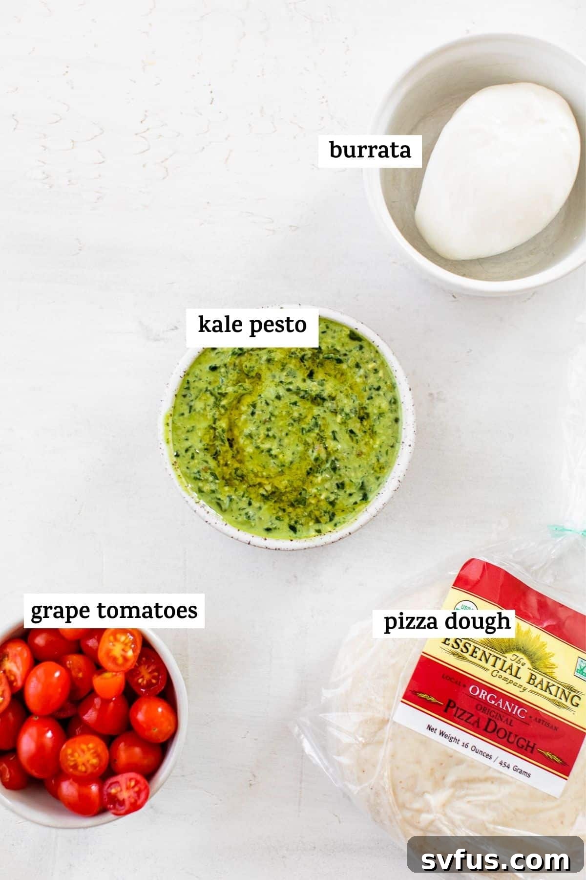 Fresh ingredients for Kale Pesto Pizza arranged on a cutting board, including kale pesto, tomatoes, and burrata cheese.