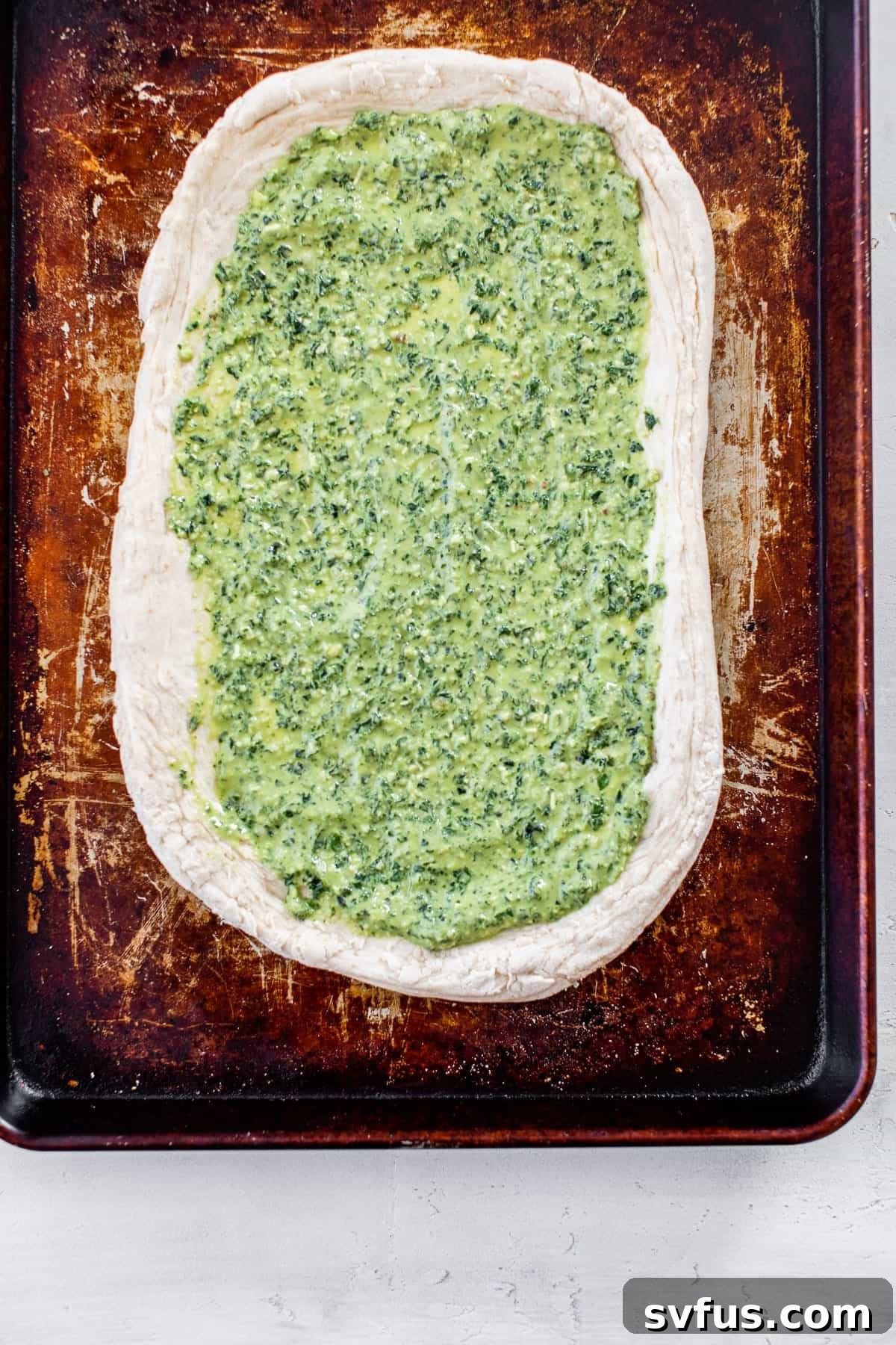 Unbaked pizza dough on a baking sheet, with vibrant kale pesto spread across the base.
