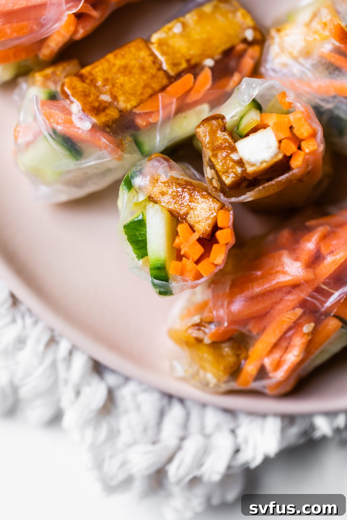 A large platter generously filled with vibrant and perfectly rolled sesame tofu spring rolls, served with a selection of tempting dipping sauces for a delicious meal.