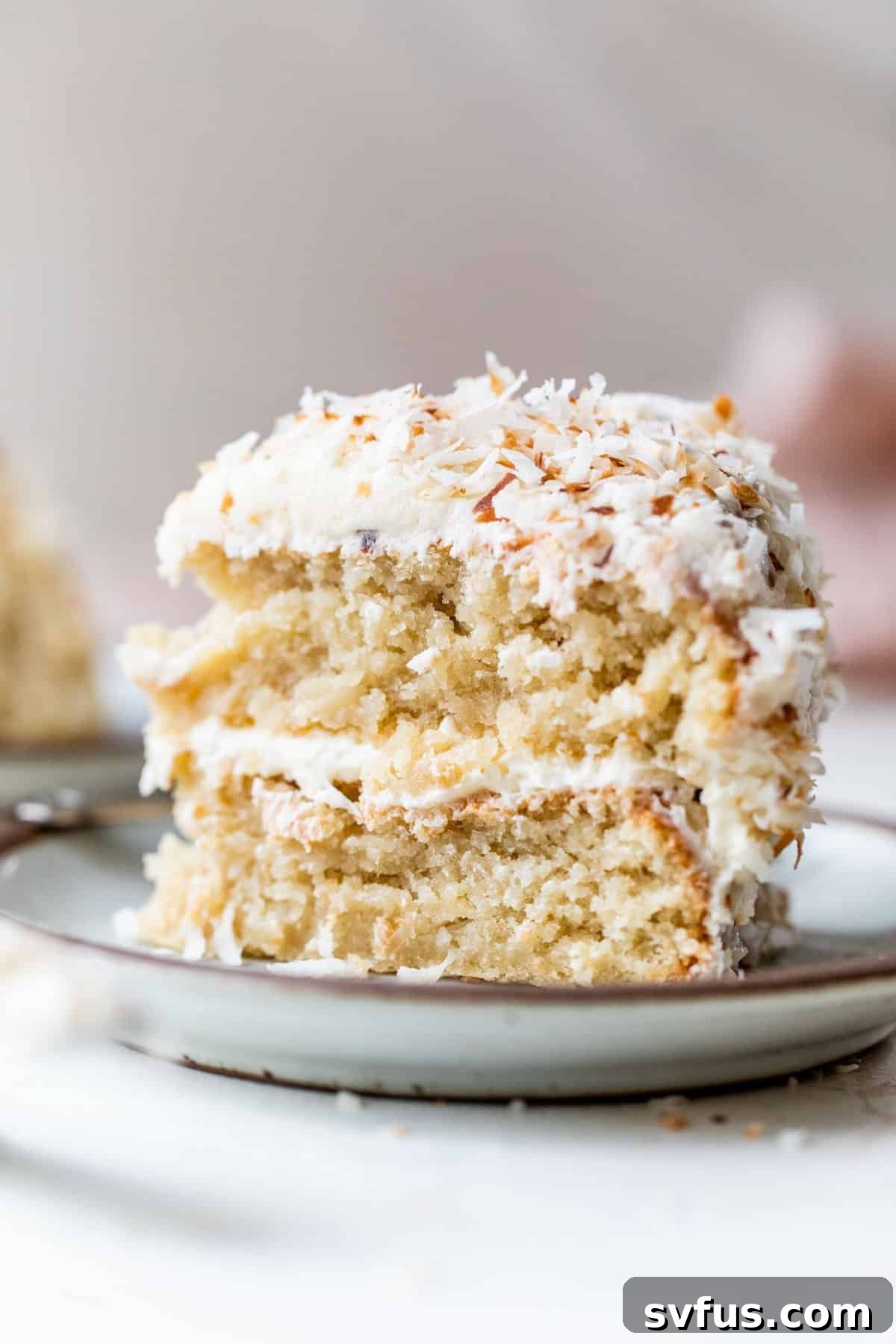 A beautifully sliced vegan coconut cake on a plate, topped with creamy white icing and shredded coconut. A perfect blend of texture and flavor.