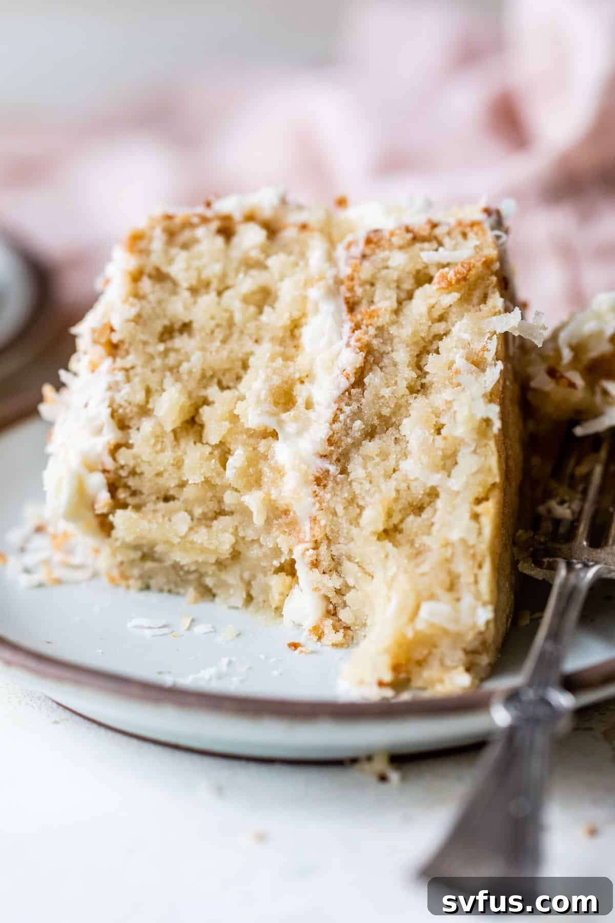 A tantalizing slice of vegan coconut cake on a plate with a bite taken out, revealing its moist layers and creamy frosting.