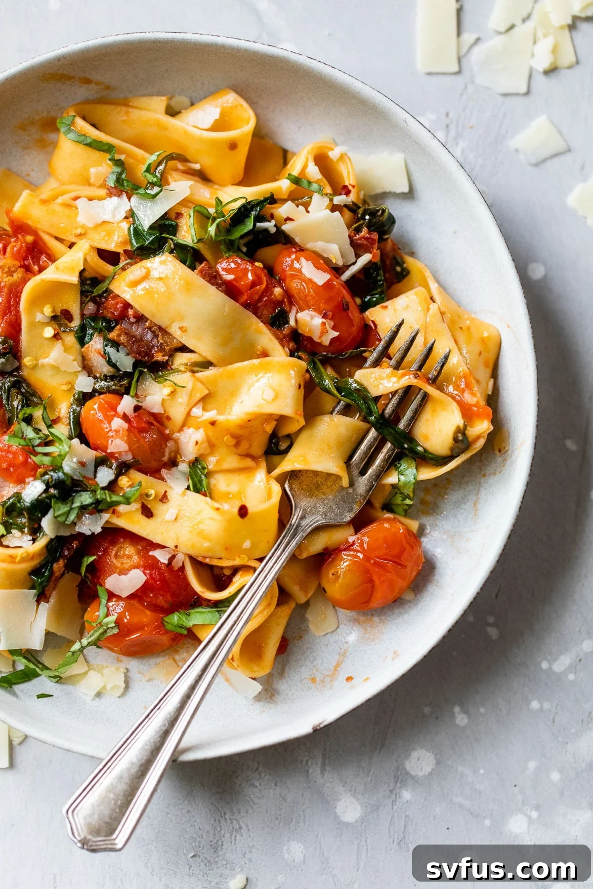 A beautifully plated bowl of long cooked pasta generously topped with vibrant grape tomatoes and freshly chopped basil, promising a burst of fresh flavor.