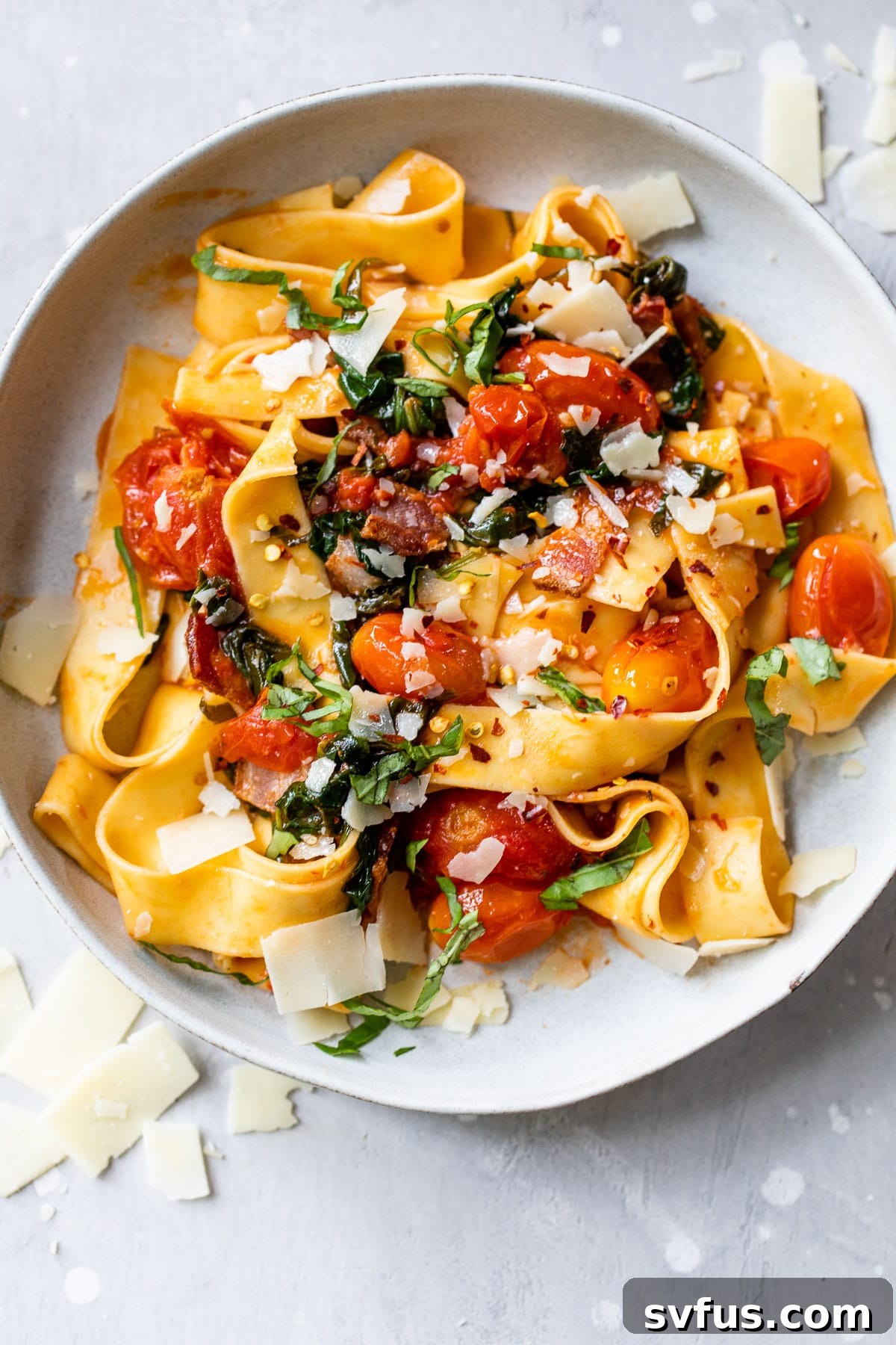 A vibrant bowl of garlic tomato pasta, elegantly garnished with crispy bacon, fresh basil leaves, and grated Parmesan cheese, ready to be enjoyed.