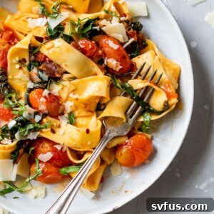 long cooked pasta in a bowl with grape tomatoes and chopped basil