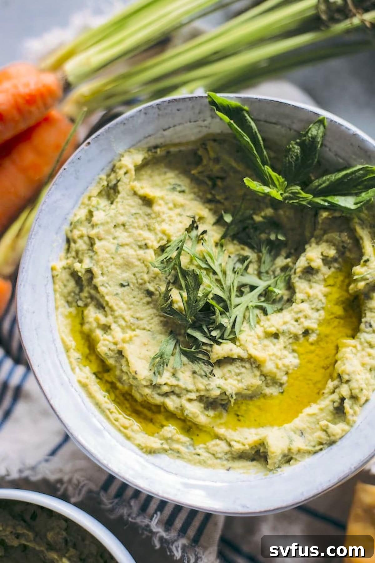 A bowl of vibrant green carrot top pesto hummus, garnished with fresh basil leaves, ready to be served.