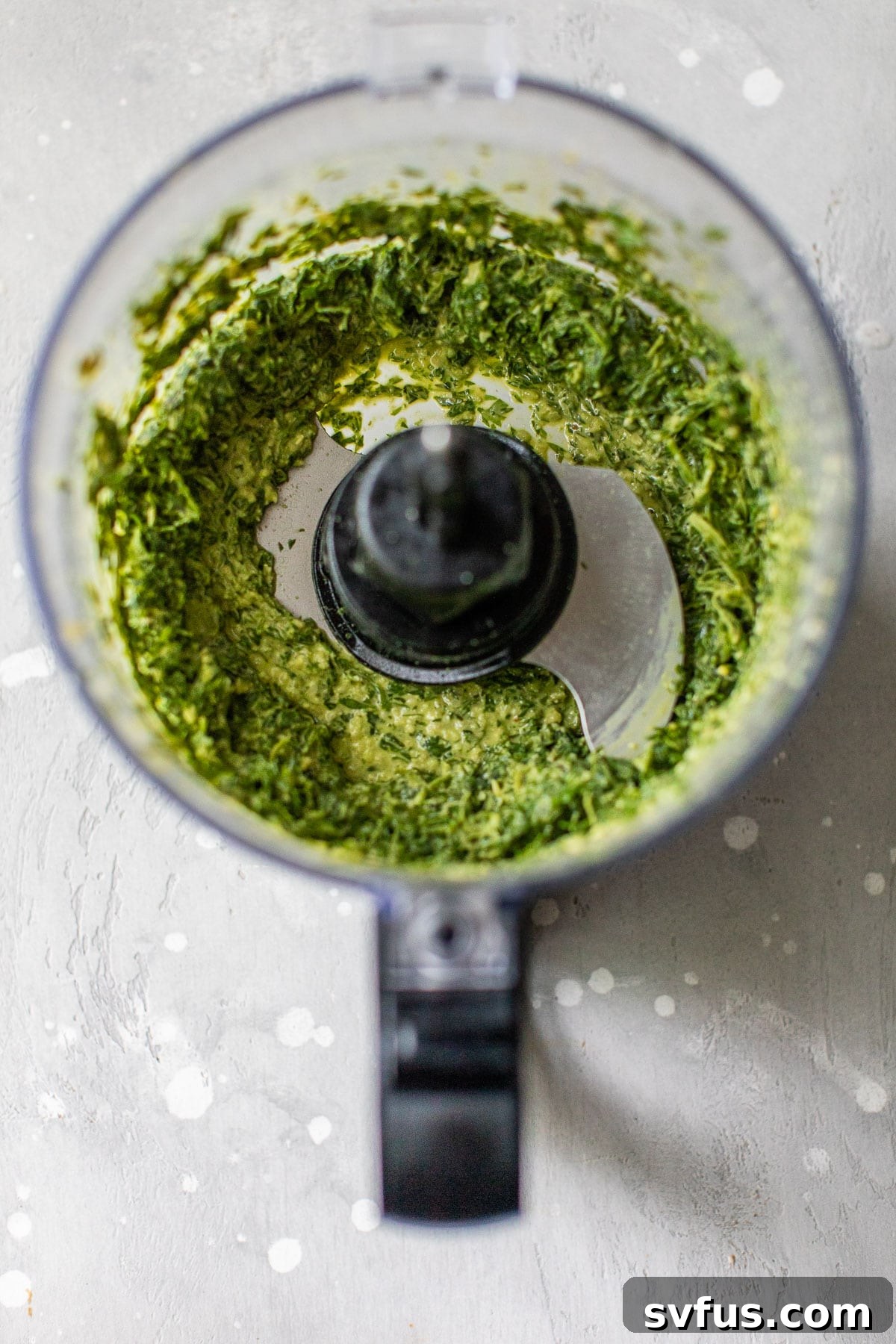 Close-up shot of homemade carrot top pesto being blended in a food processor, showing its bright green color and smooth texture.