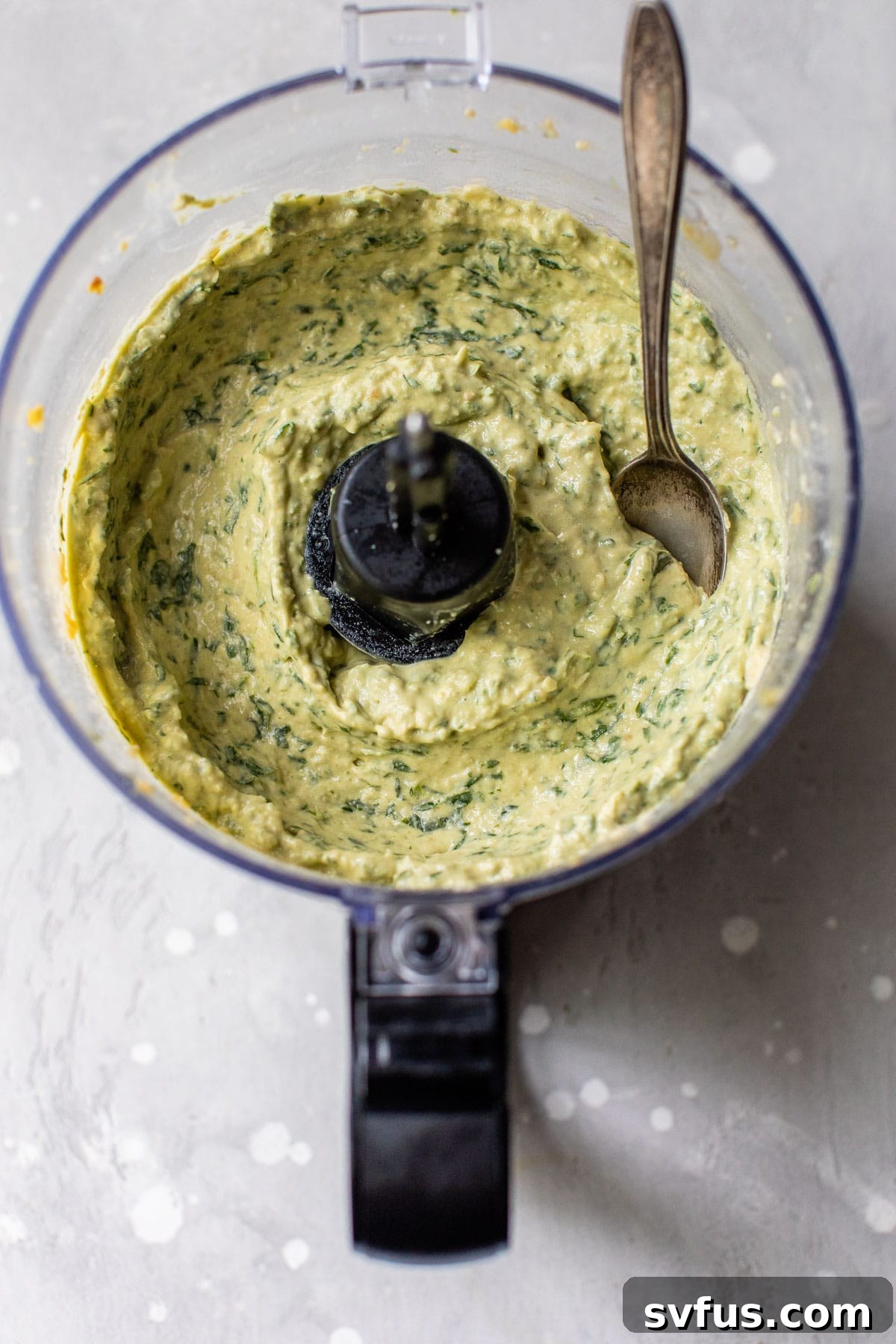 A mix of vibrant green pesto and creamy hummus being combined in a food processor, creating a swirled effect.
