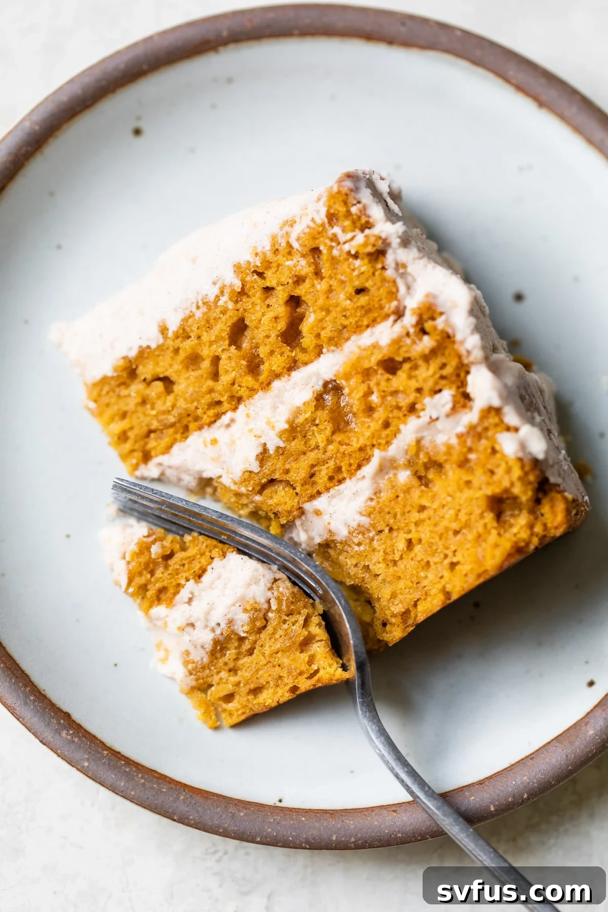 A beautifully presented slice of Vegan Pumpkin Cake on a white plate, showcasing its moist texture and cinnamon buttercream layers.