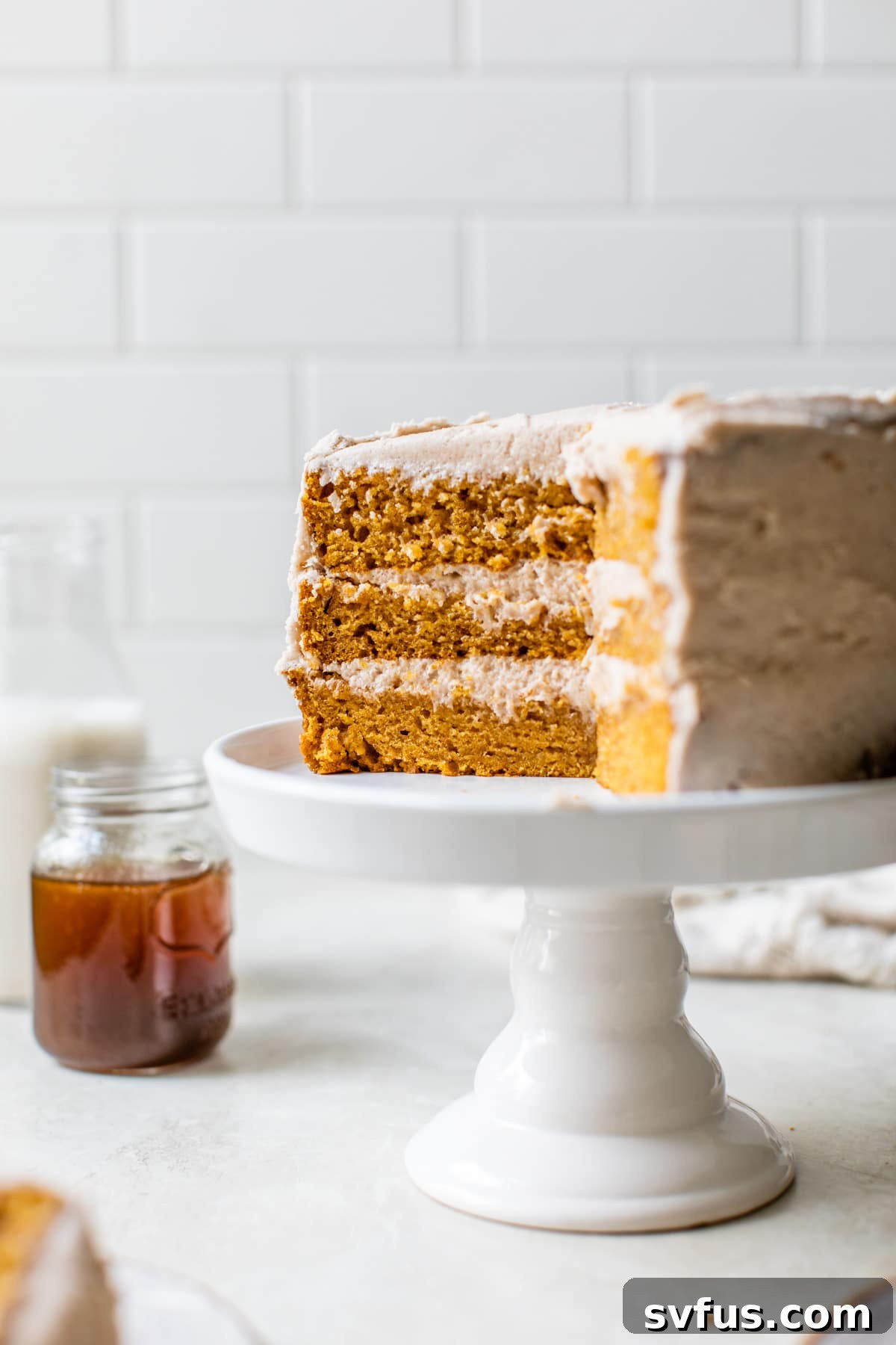 A stunning three-tier Vegan Pumpkin Cake adorned with cinnamon buttercream and a light drizzle of caramel sauce, presented on a white cake stand.