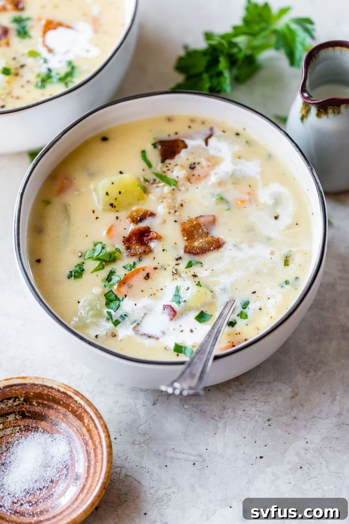 A generously sized bowl of creamy potato barley soup, garnished with crispy bacon bits and fresh herbs, ready to be enjoyed.