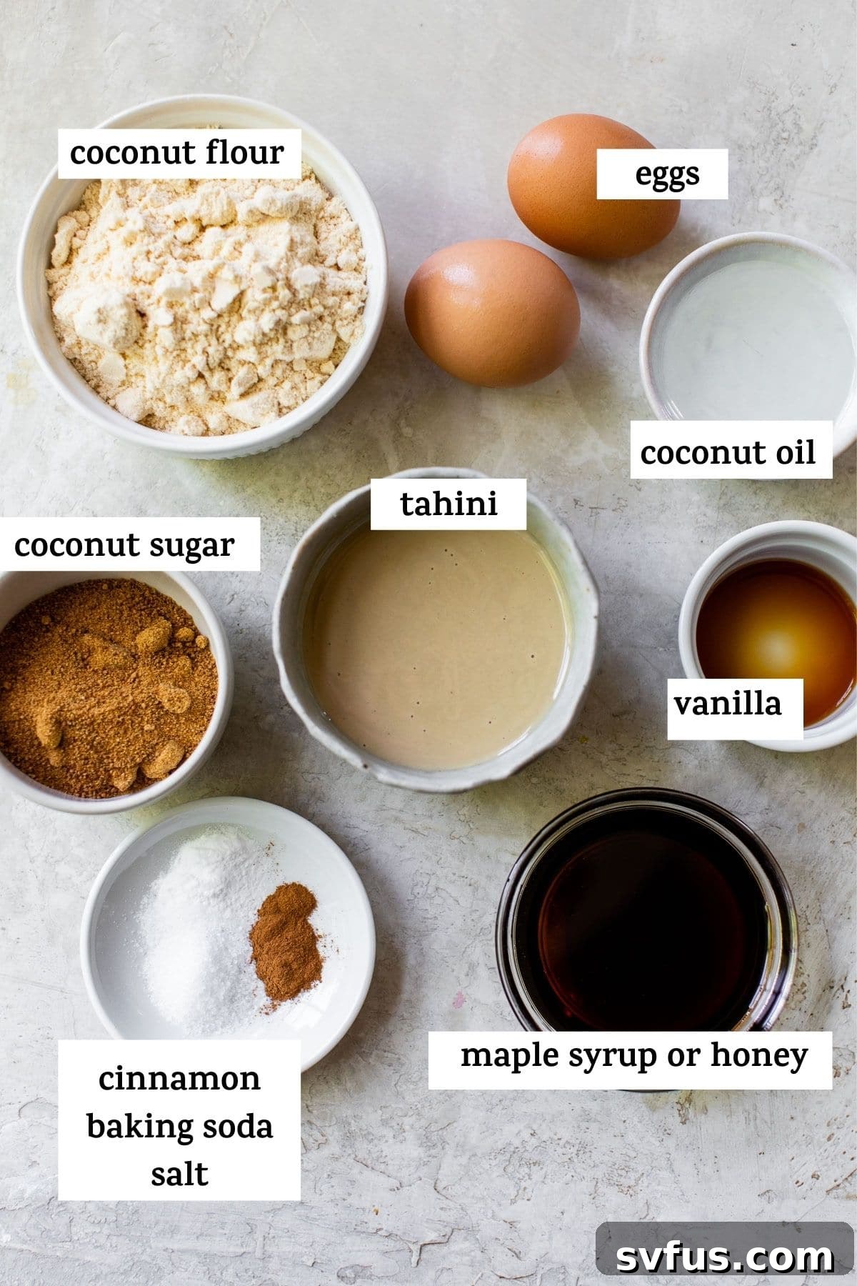 Various ingredients laid out on a table, including tahini, eggs, honey, coconut oil, coconut flour, chocolate chips, and spices, with text overlay.