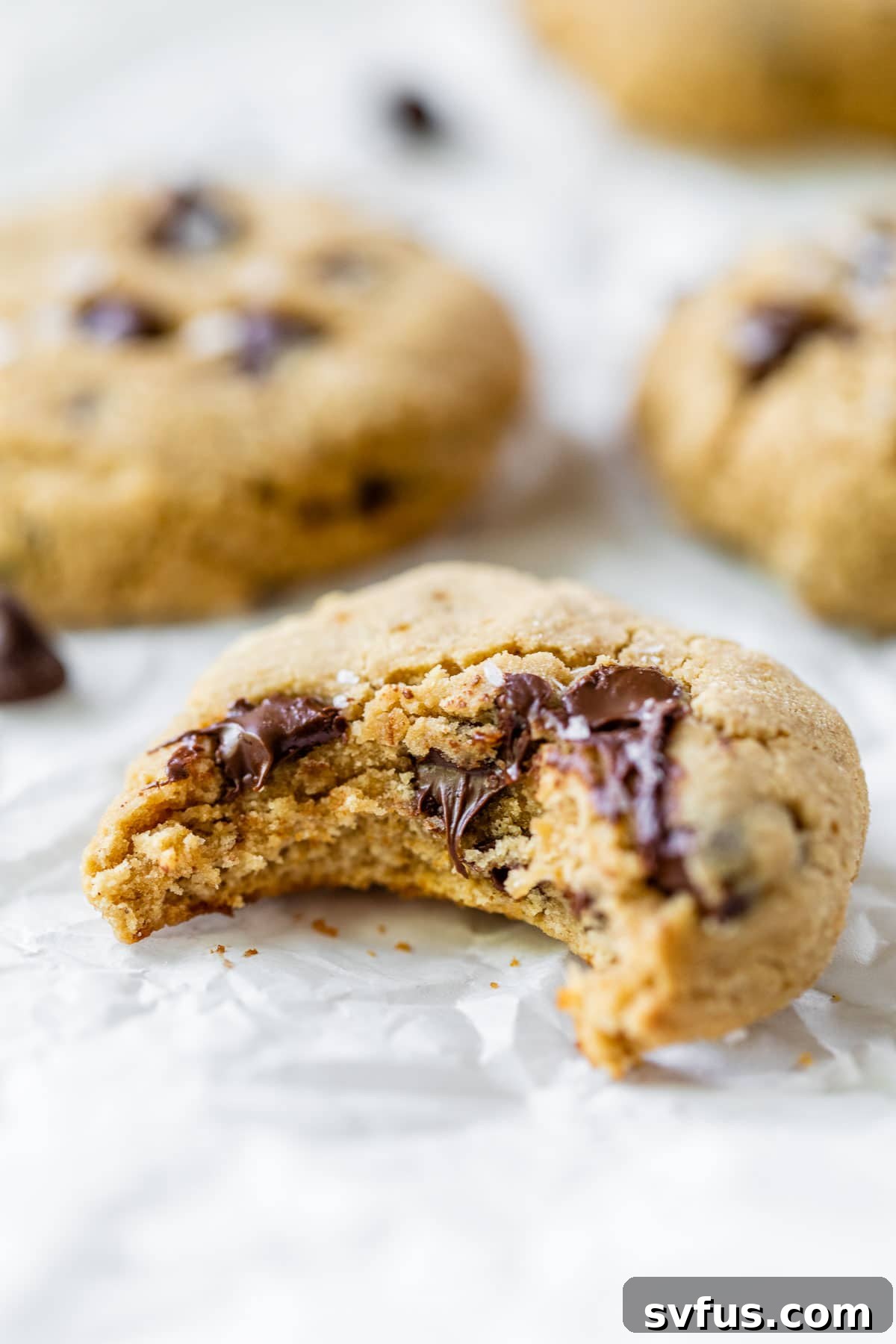 A perfectly baked gluten-free tahini chocolate chip cookie with a bite taken out, showing its chewy interior and melted chocolate.