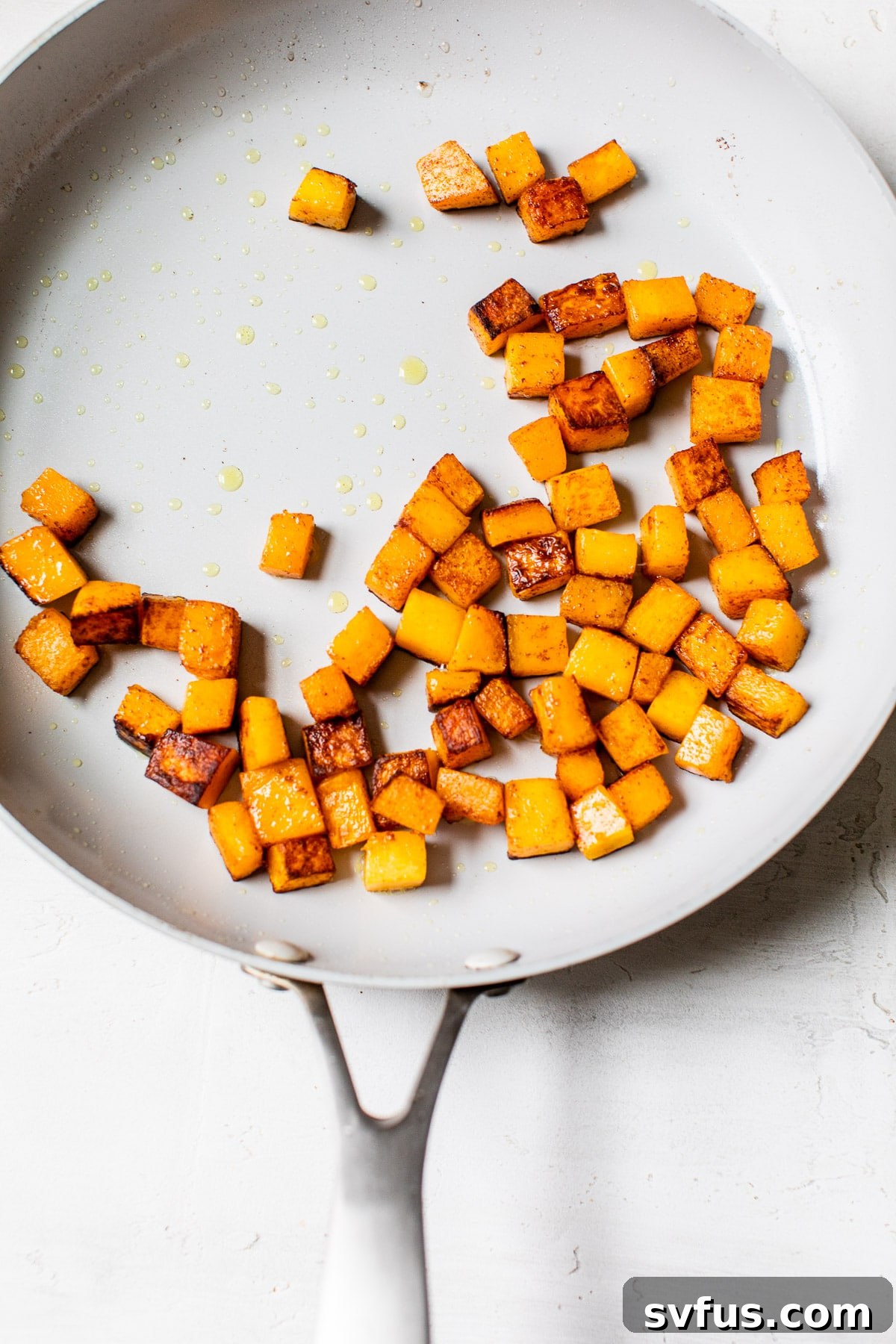 Close-up of cubed butternut squash sizzling in a large skillet, lightly browned and spiced with cinnamon, as part of the salad preparation.
