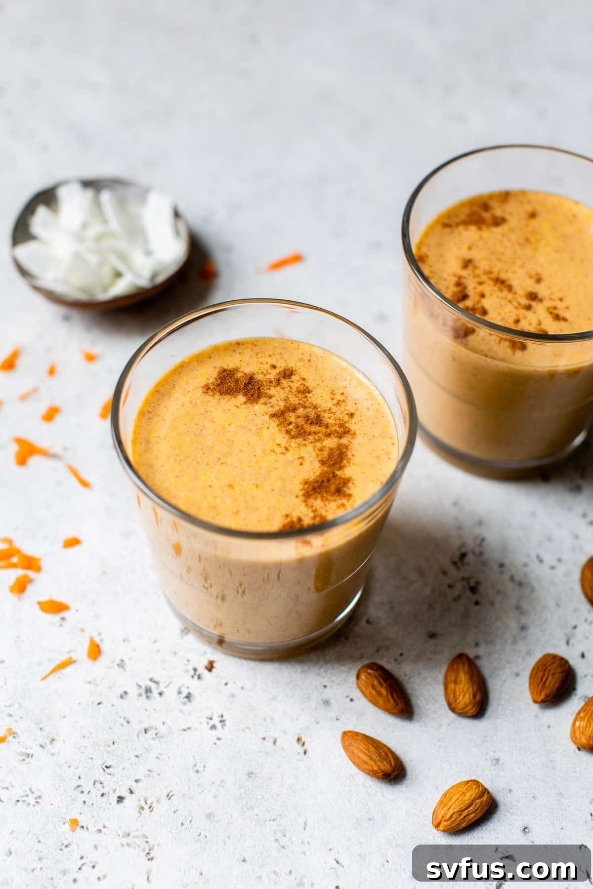 Smoothie on a table garnished with almonds and shredded coconut, evoking a carrot cake aesthetic