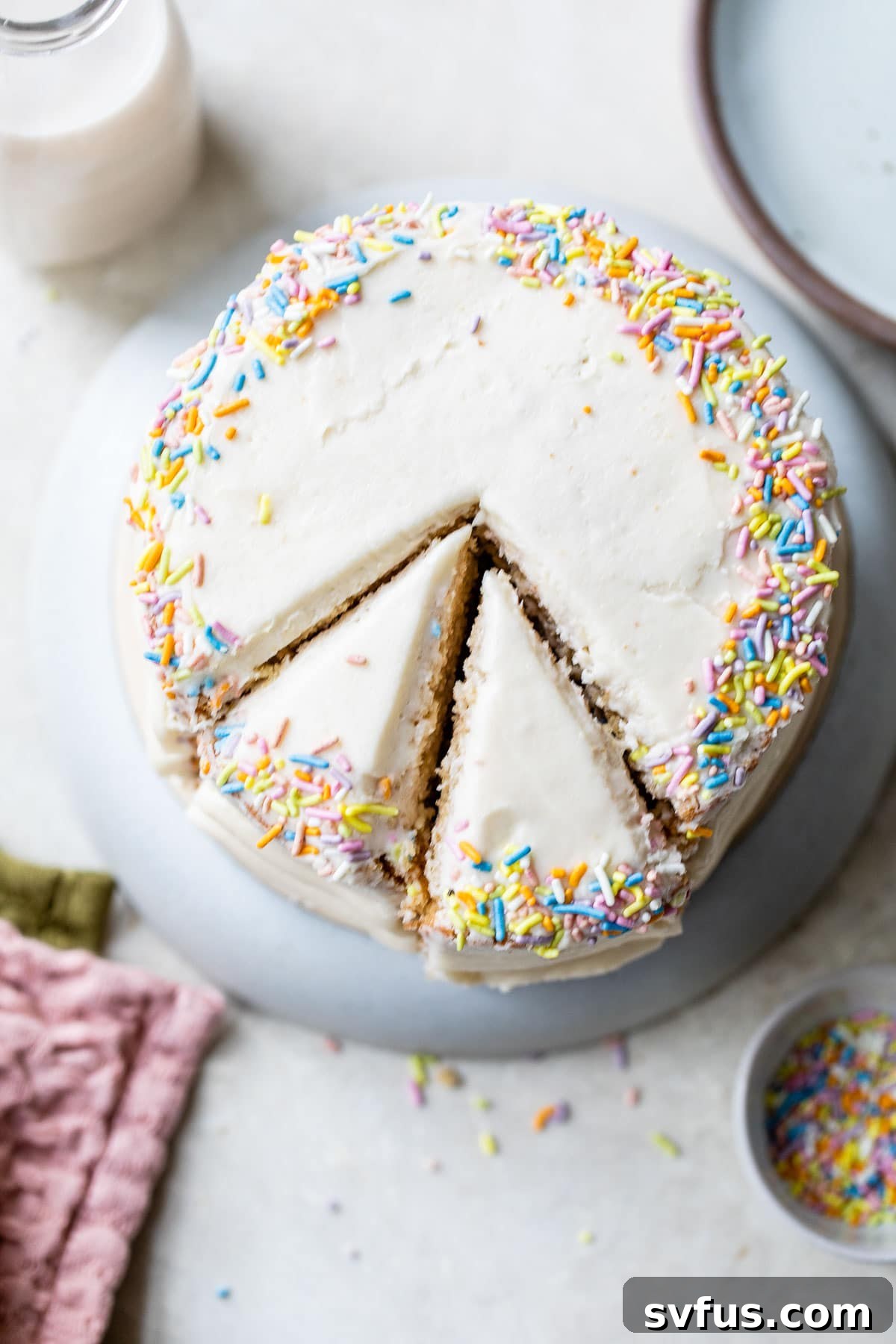 An overhead shot of a beautifully frosted vegan vanilla cake, topped with colorful sprinkles, ready to be enjoyed.