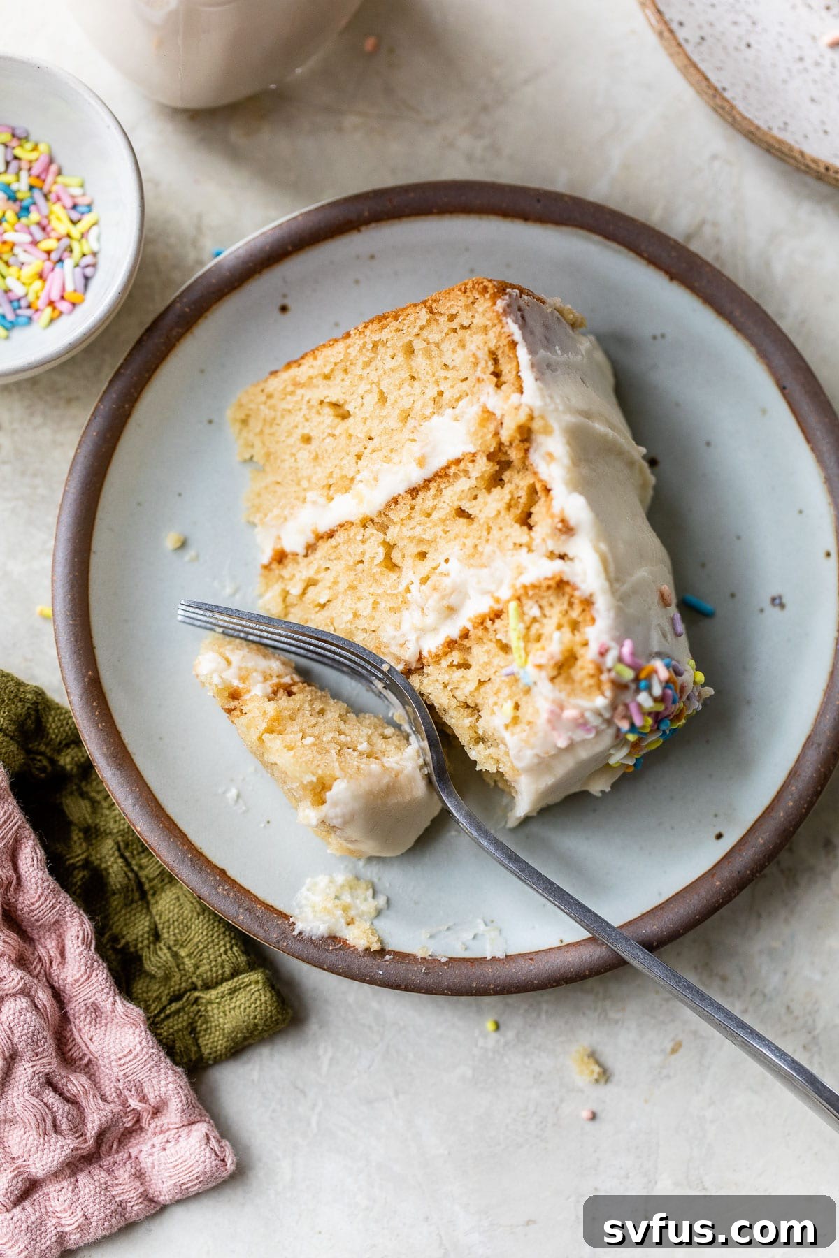 A perfect slice of moist vegan vanilla cake on a white plate, showcasing its tender crumb and creamy frosting.