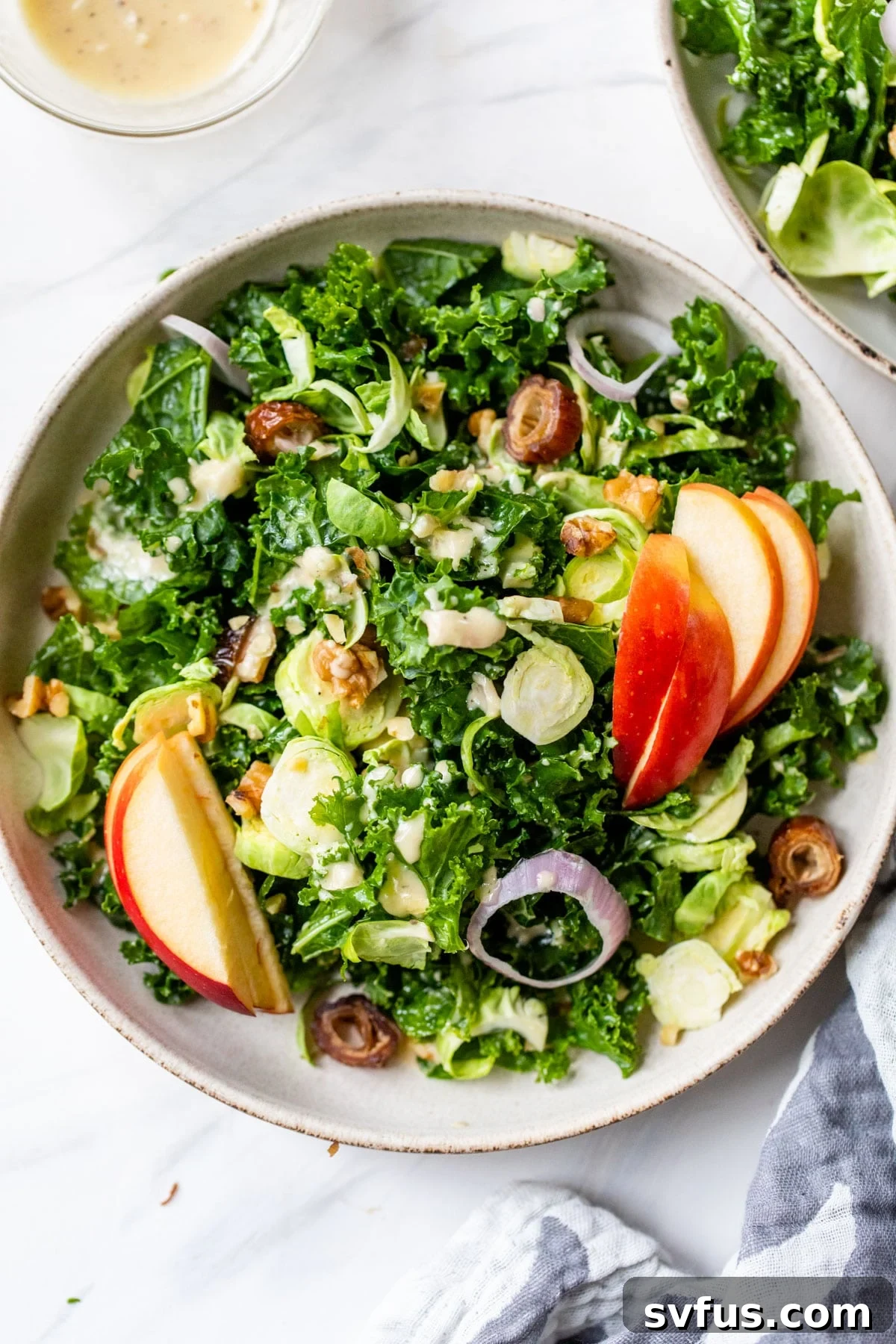 A beautifully presented bowl of fresh kale, apple, and Brussels sprouts salad, garnished with finely sliced shallots and crunchy walnuts, ready to be served as a healthy and colorful winter side dish.