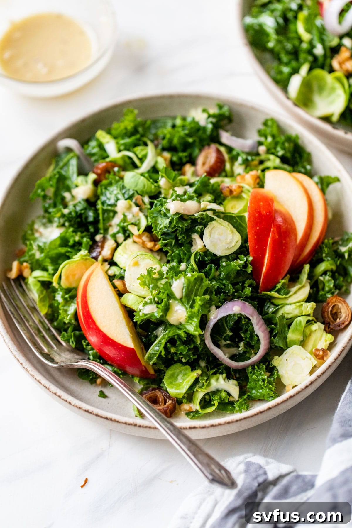 A large serving bowl filled with a fresh, colorful kale, apple, and Brussels sprouts salad, showcasing the beautifully mixed ingredients and the glistening dressing, ready to be enjoyed.