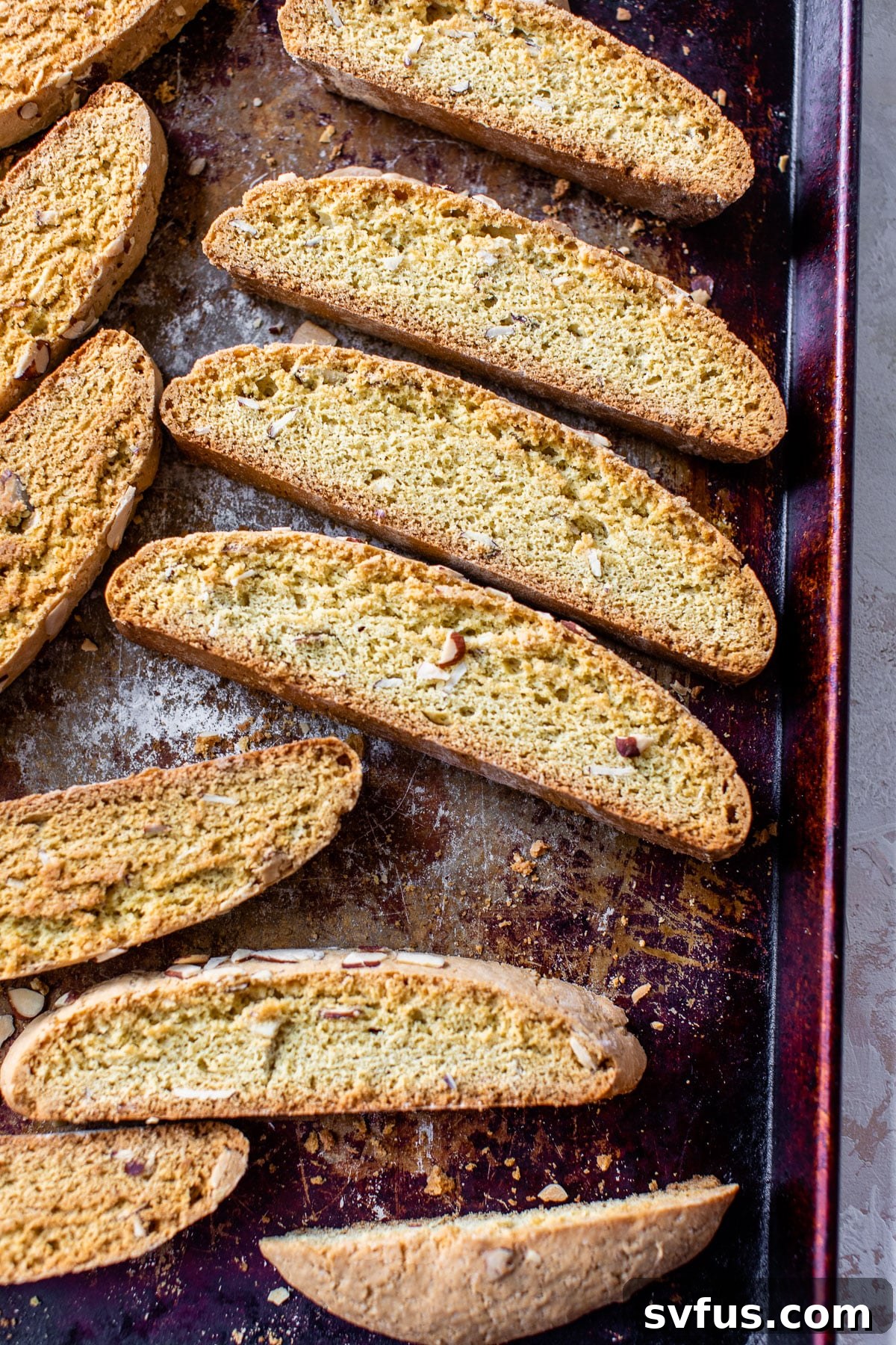 Rows of perfectly sliced and twice-baked almond biscotti cooling on a baking sheet, ready for chocolate dipping.