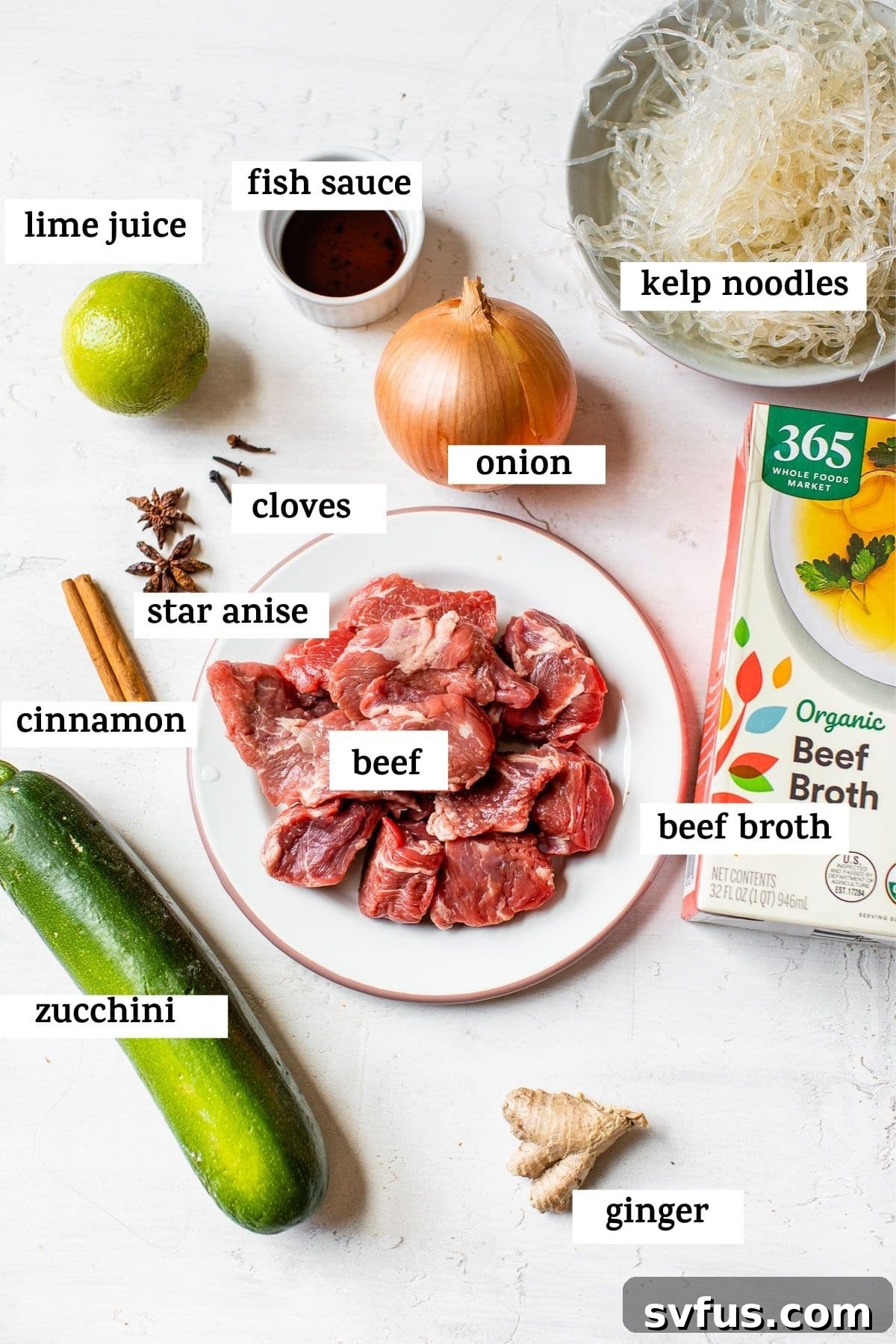A flat lay image showing all the fresh ingredients required for Paleo Beef Pho, including beef, zucchini, kelp noodles, ginger, onion, and various spices.