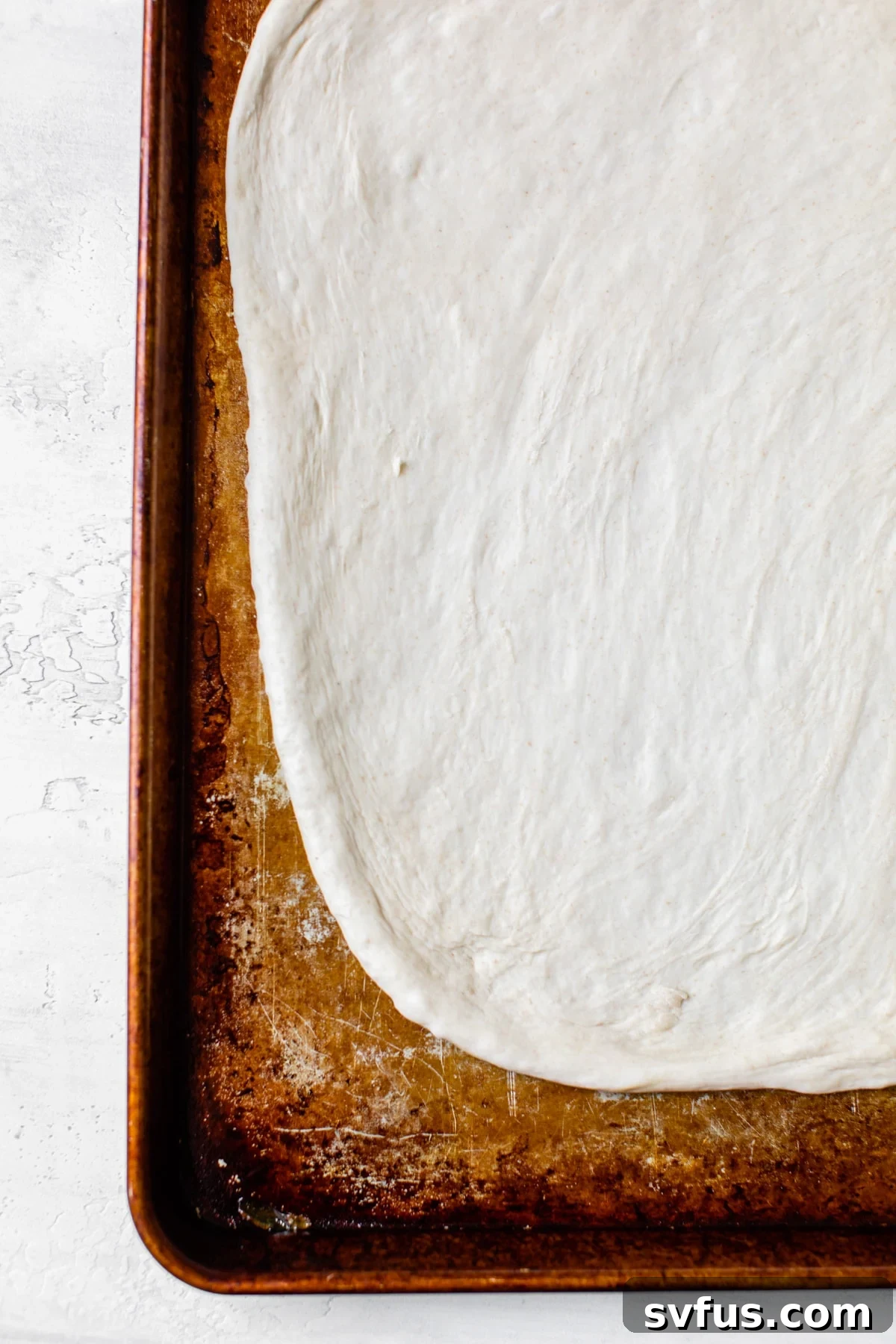 Fresh pizza dough rolled out and placed on a baking sheet, ready for toppings.