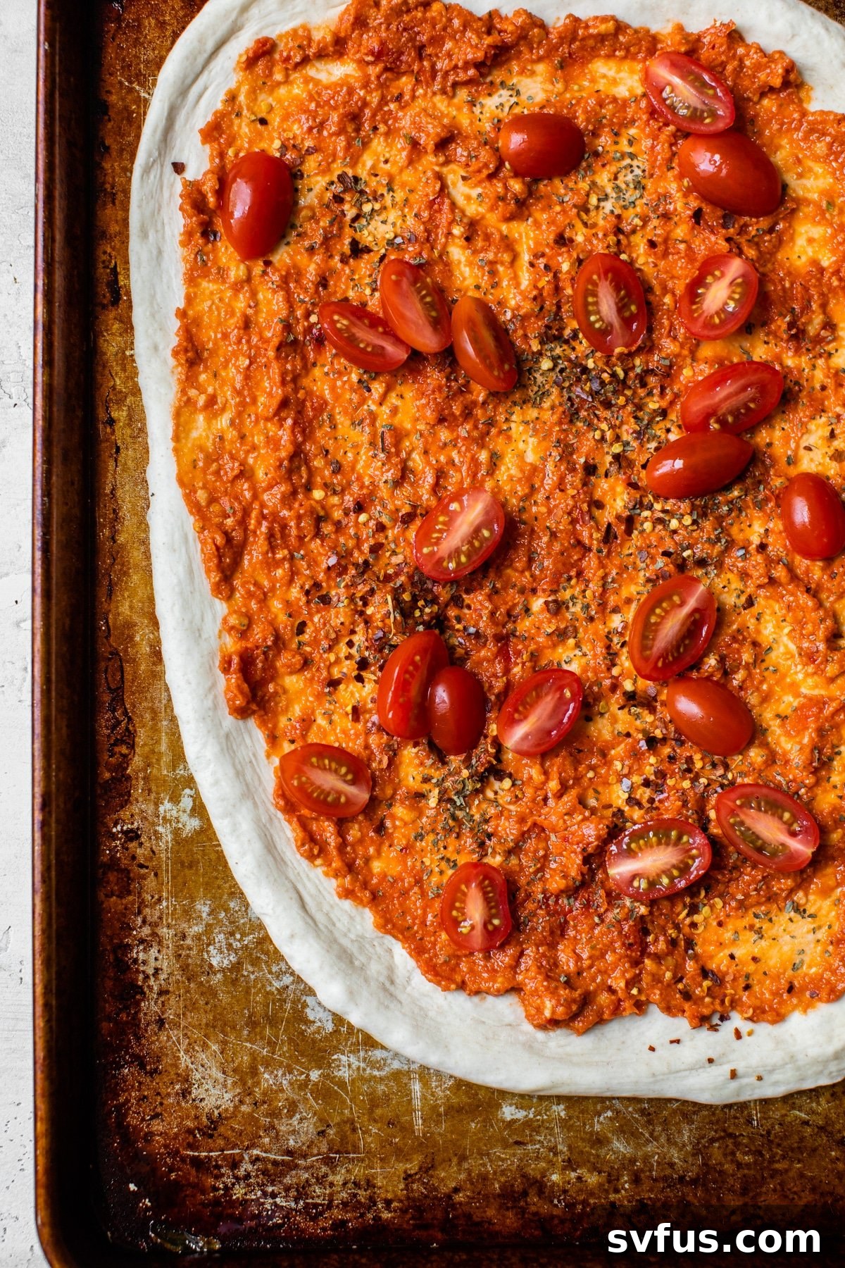 Pizza dough covered with sun-dried tomato pesto and initial seasonings, ready for baking.
