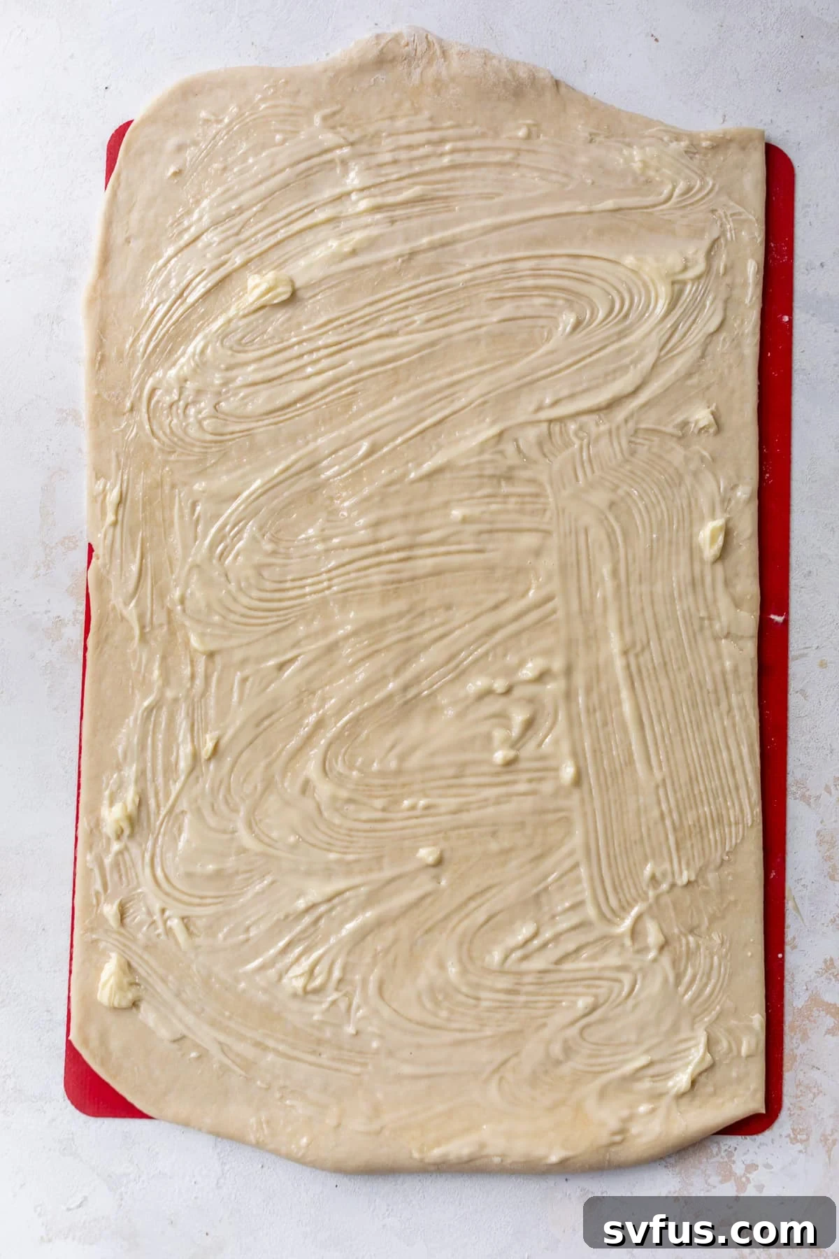 Overhead view of a rectangle of vegan cinnamon roll dough generously slathered with softened vegan butter.