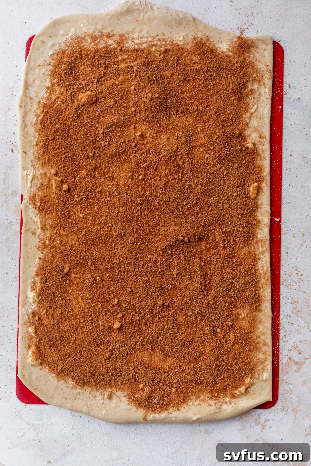 Overhead view of a rectangle of vegan cinnamon roll dough topped with a uniform layer of cinnamon sugar mixture.
