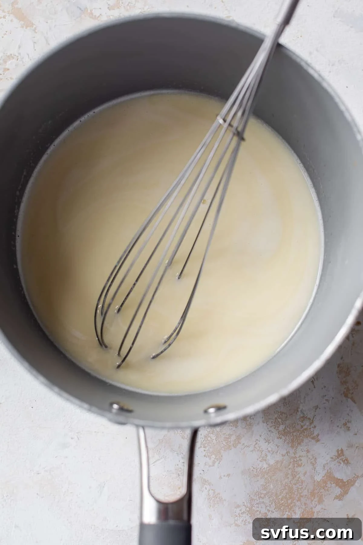 Overhead view of a whisk stirring a melted vegan butter and non-dairy milk mixture in a saucepan.