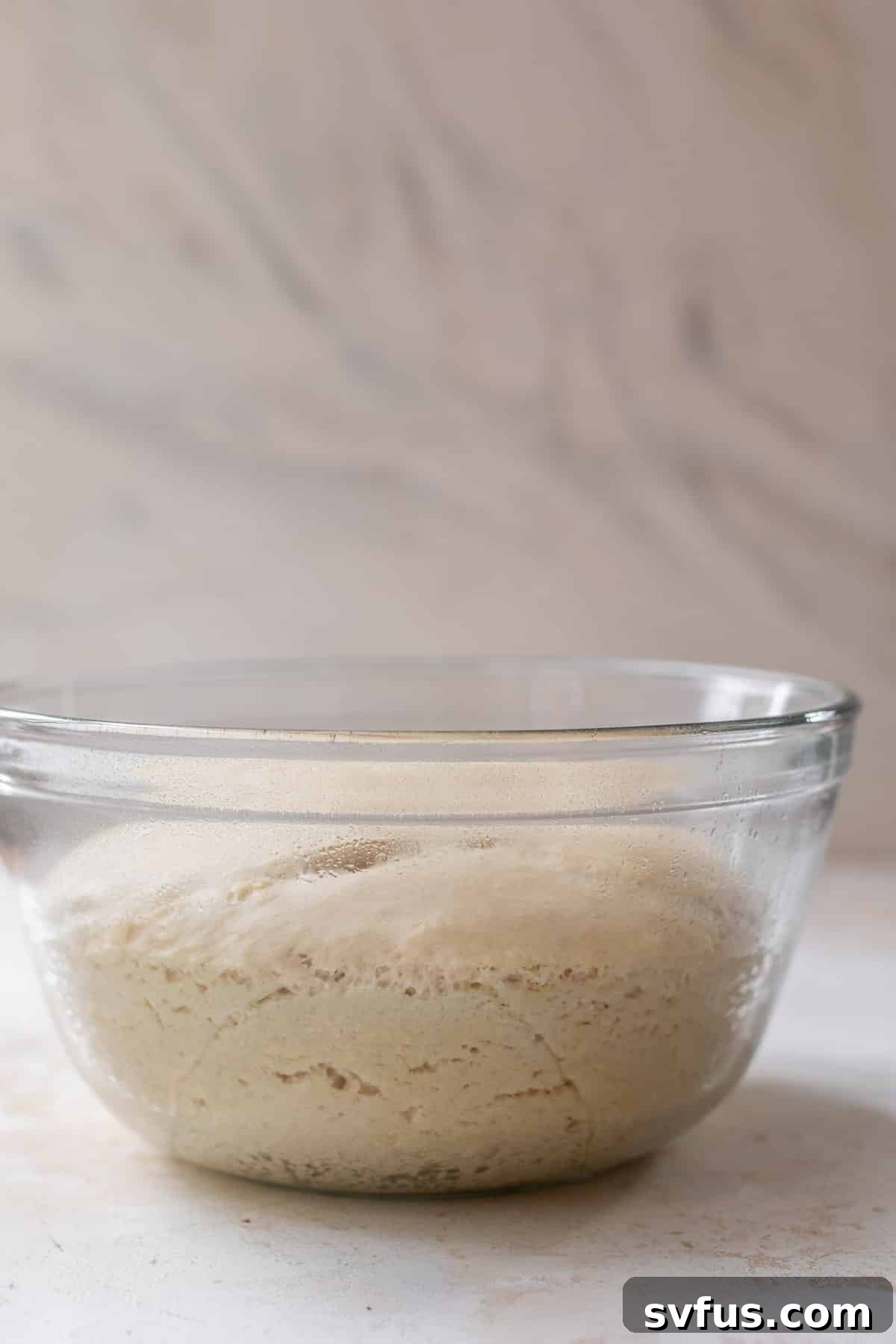 Side view of beautifully risen vegan cinnamon roll dough in a glass bowl, having doubled in size.