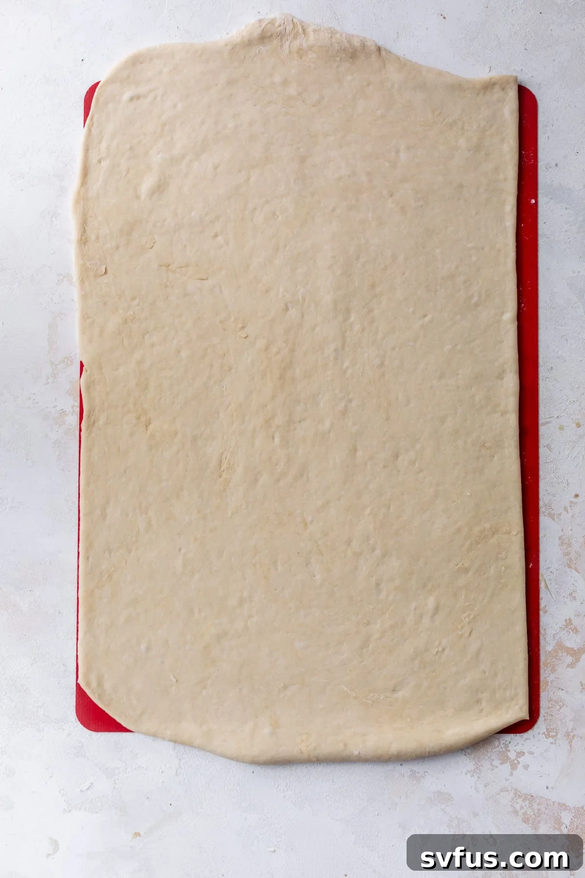Overhead view of vegan cinnamon roll dough perfectly rolled out into a neat rectangle on a baking mat.