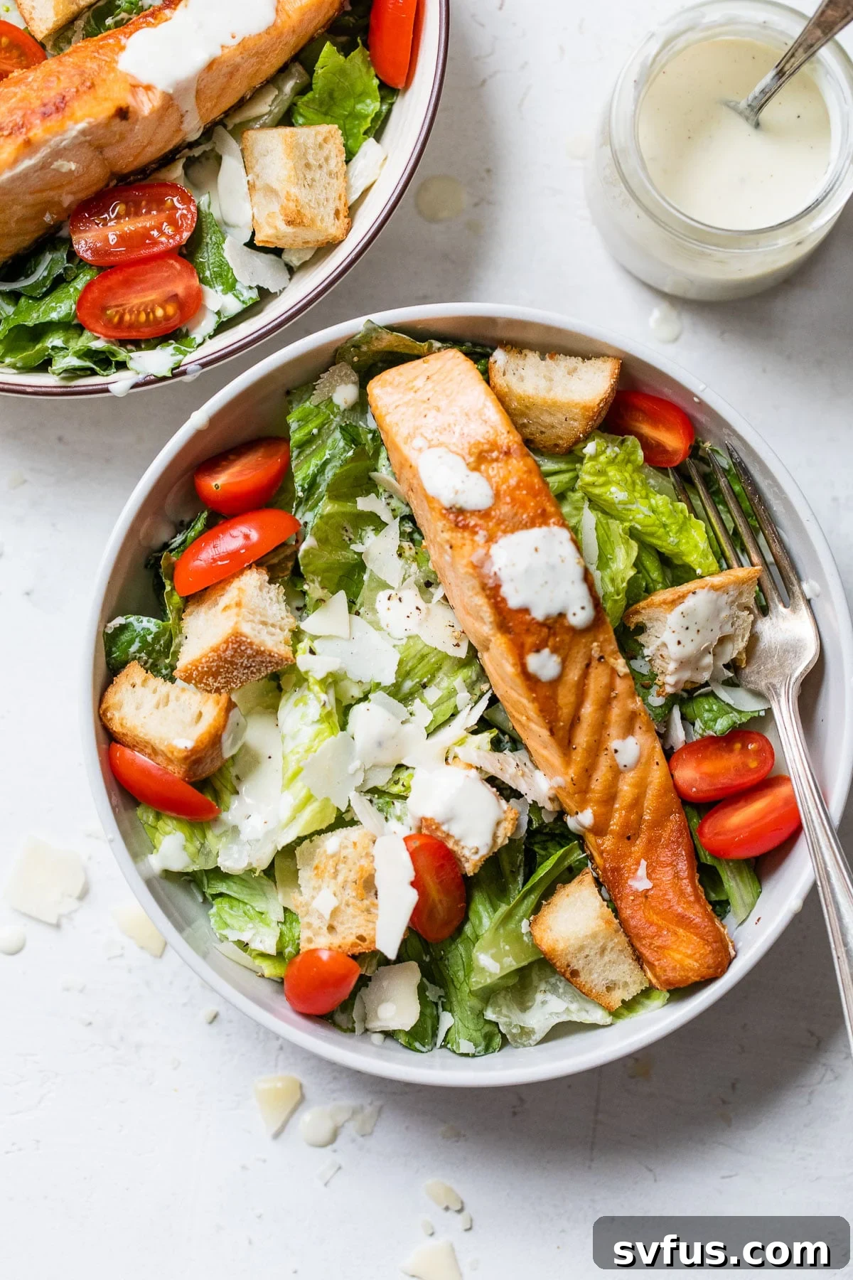 A vibrant bowl of fresh romaine lettuce topped with bright red grape tomatoes and perfectly cooked salmon fillets, ready to be dressed.