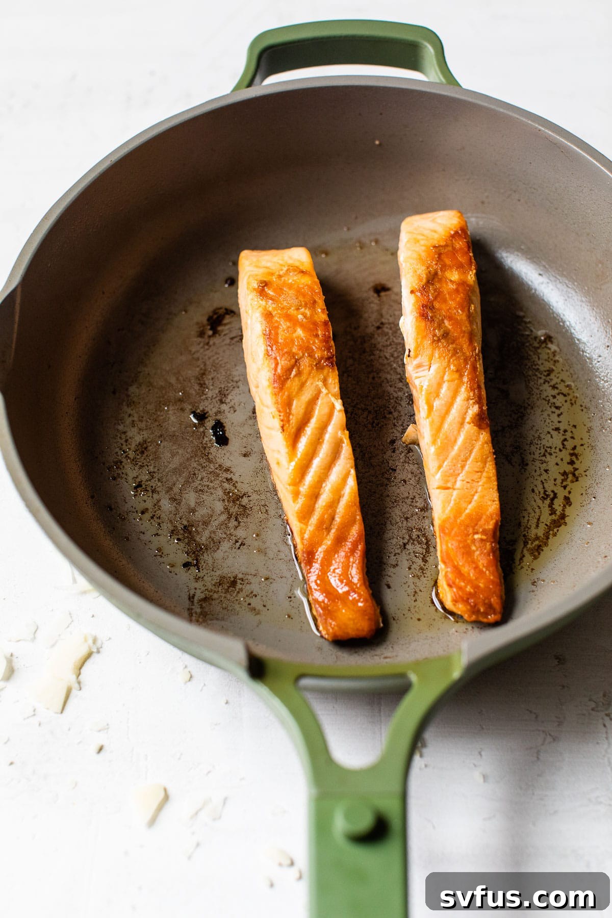 A close-up shot of perfectly cooked salmon fillets in a nonstick skillet, exhibiting a beautiful golden-brown sear.