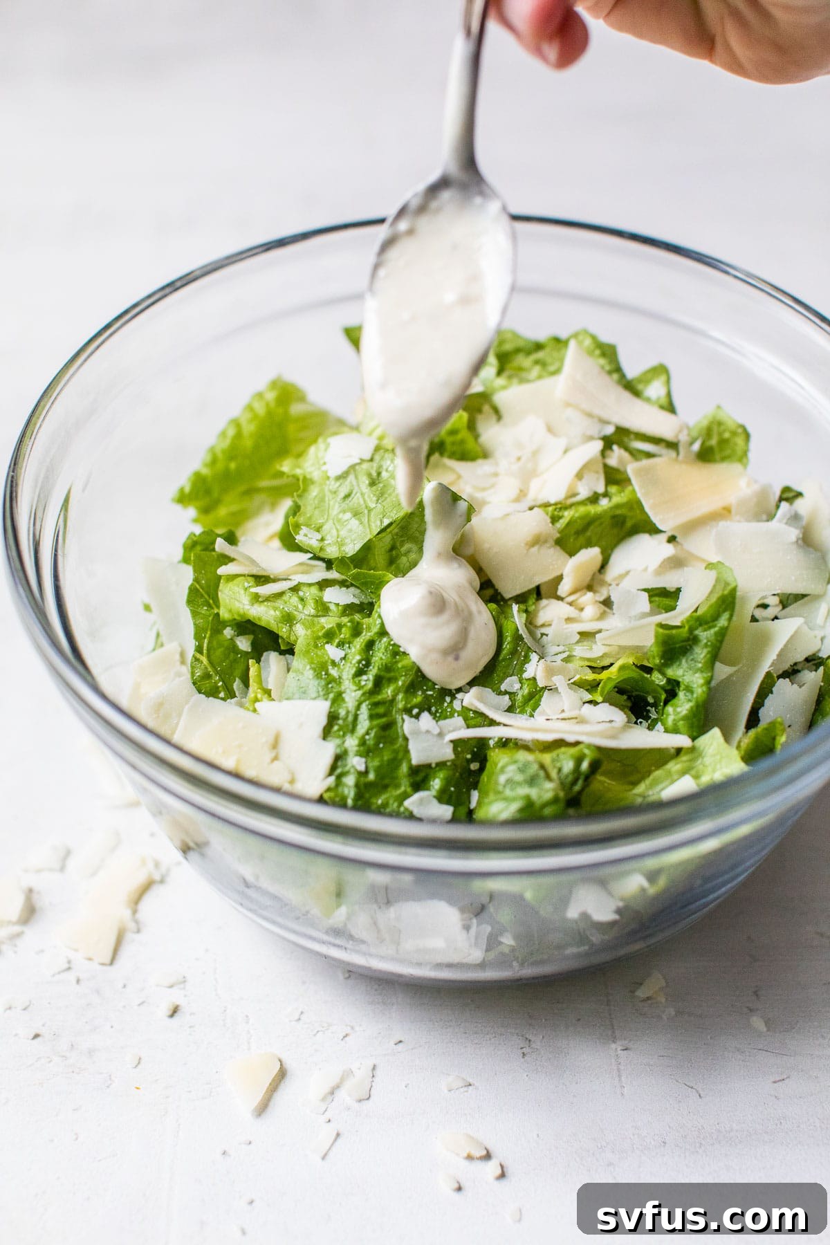 A large mixing bowl filled with crisp romaine lettuce, lightly drizzled with homemade Caesar dressing, ready to be tossed.