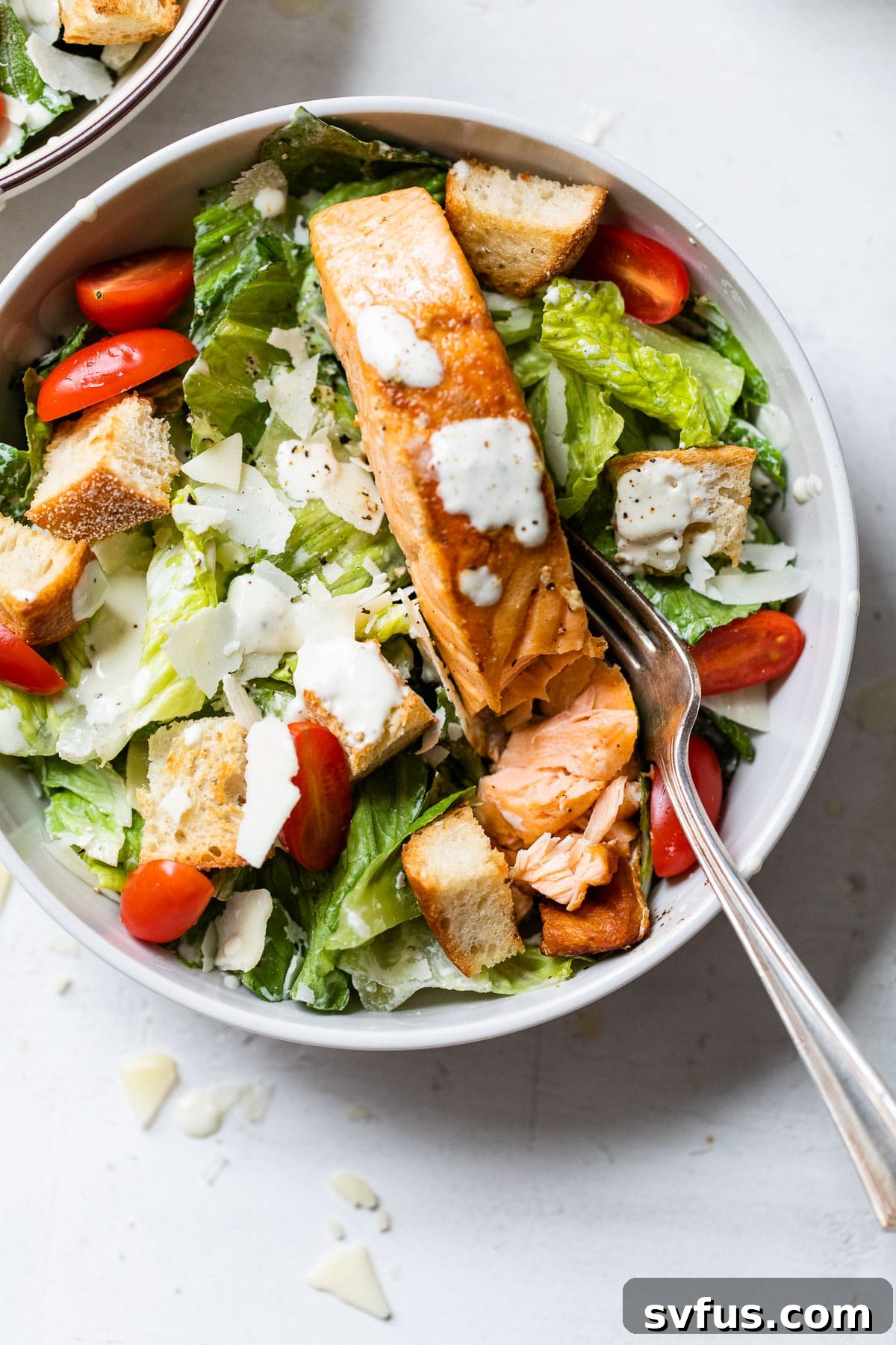 A beautifully presented bowl of Salmon Caesar Salad, featuring crisp lettuce, bright tomatoes, crunchy croutons, and a generous fillet of pan-seared salmon.