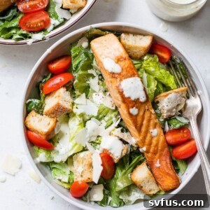 A vibrant bowl of fresh romaine lettuce topped with bright red grape tomatoes and perfectly cooked salmon fillets, ready to be dressed.