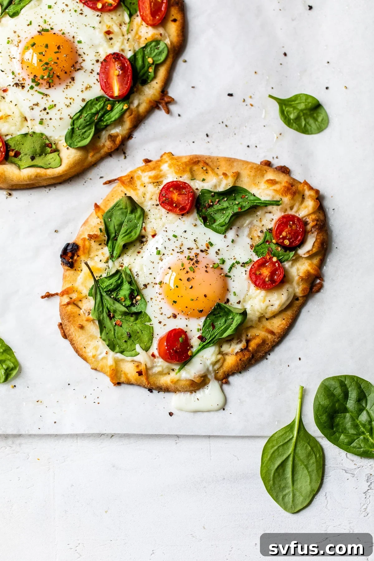 Delicious mini breakfast pizzas on naan bread, topped with vibrant vegetables, melted cheese, and a perfectly cooked fried egg, ready for a weekend feast.