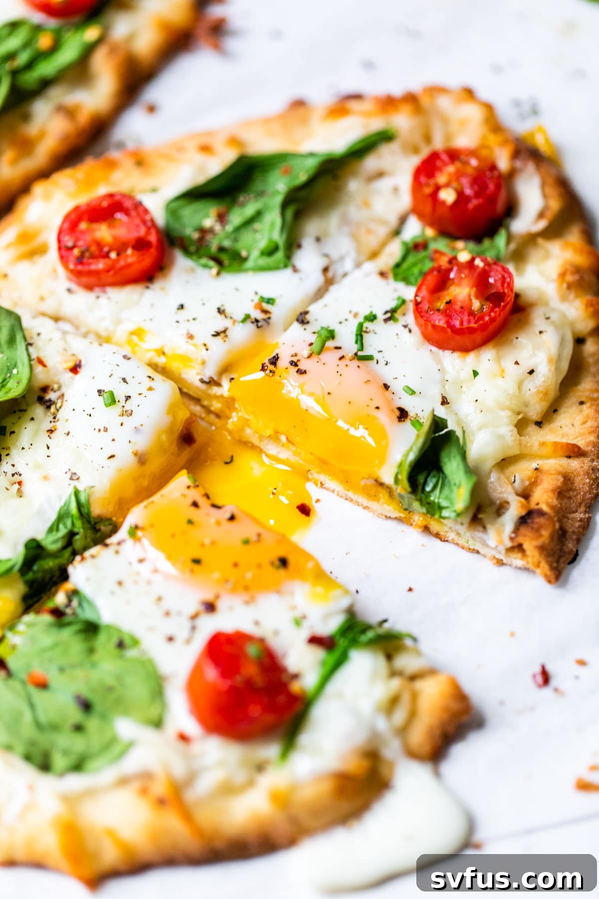 A perfectly baked mini breakfast pizza, sliced and ready to eat, showcasing a runny egg yolk, melted cheese, and fresh greens on a golden naan crust.
