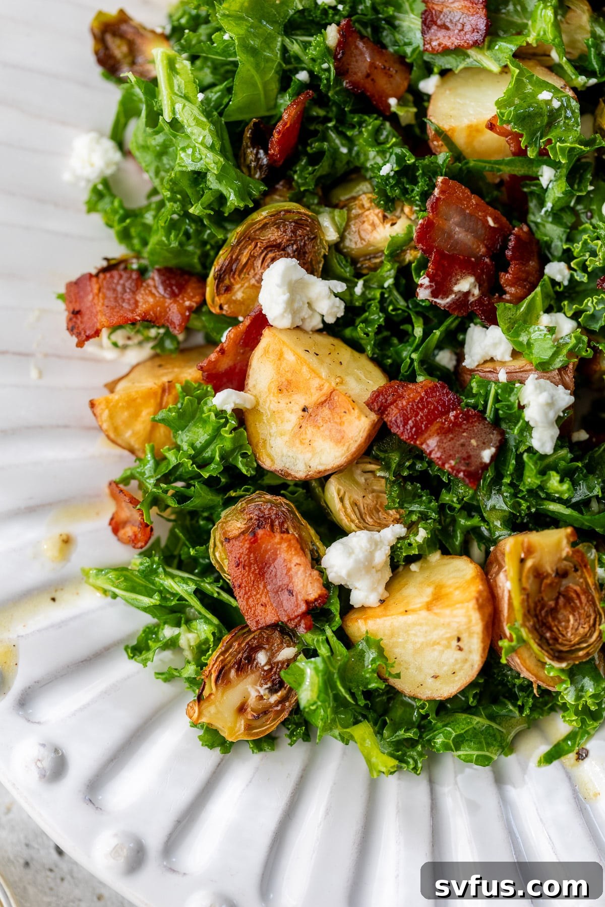 A close-up view of the Potato Brussels Sprouts Salad on a white platter, highlighting the texture of roasted vegetables, crispy bacon, and creamy goat cheese.