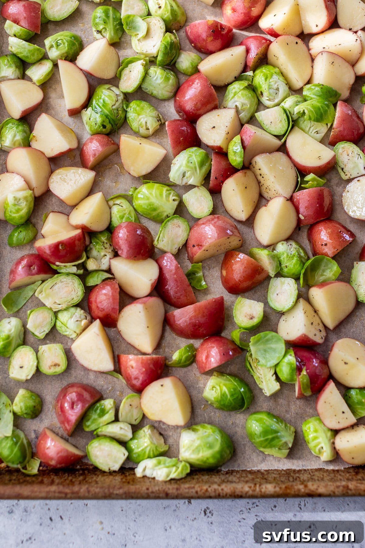 Chopped red potatoes and halved brussels sprouts are spread evenly on a baking sheet, ready for roasting, seasoned with olive oil and salt.