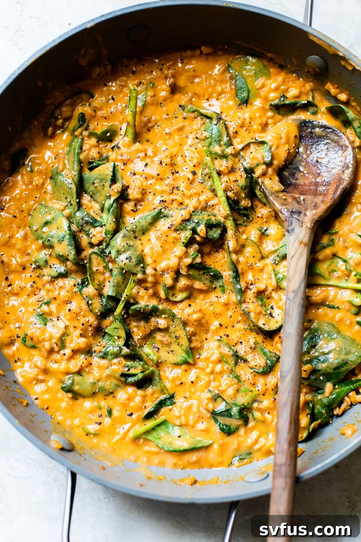 A large skillet filled with creamy Sweet Potato Curry Farro, garnished with fresh spinach.