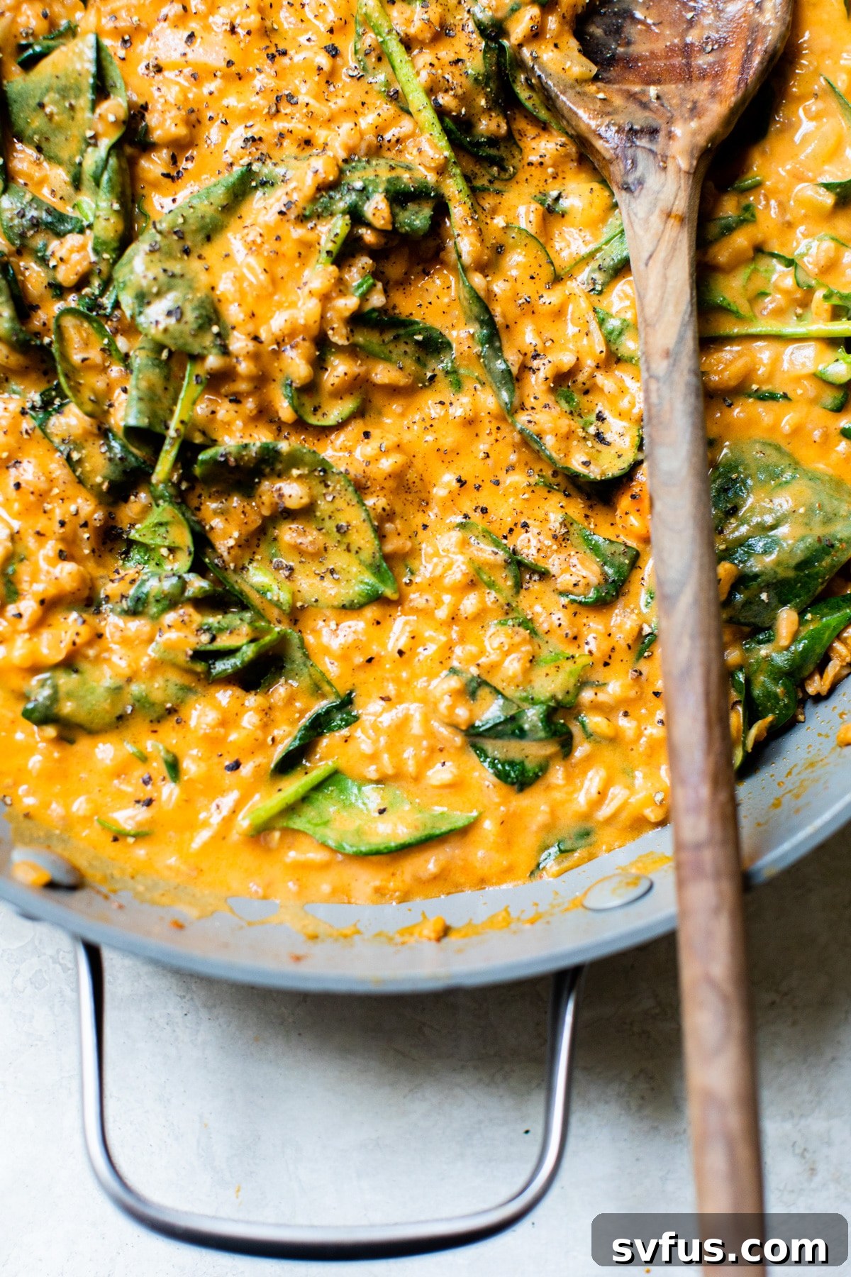 Close-up of creamy farro and spinach simmering in a rich curry broth in a skillet.