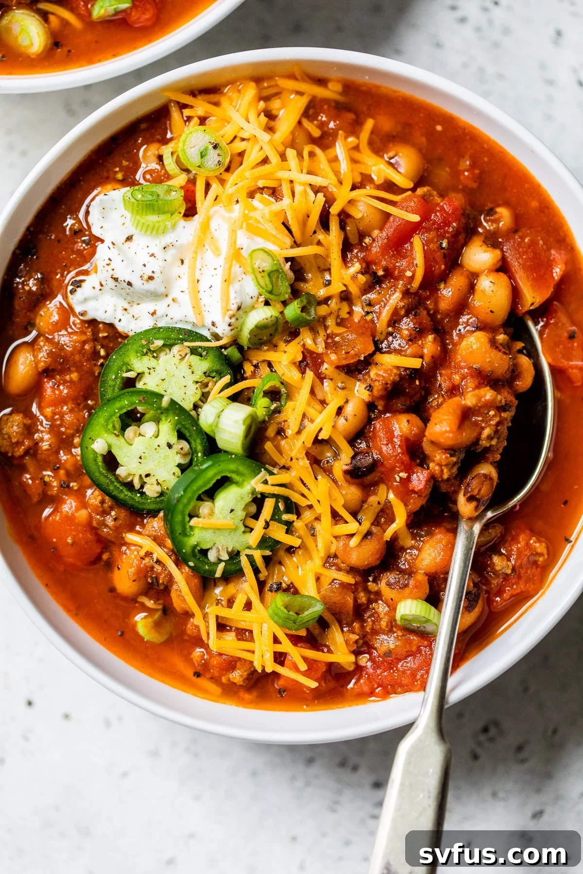 A steaming bowl of Black Eyed Peas Beer Chili, generously topped with shredded cheese and a dollop of sour cream, ready to be enjoyed.