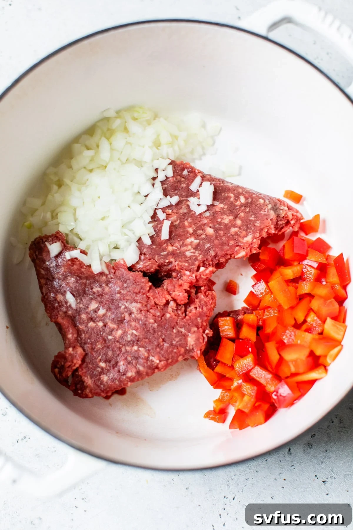 Ground beef, diced yellow onion, and red bell pepper cooking in a large Dutch oven, forming the flavor base for the chili.