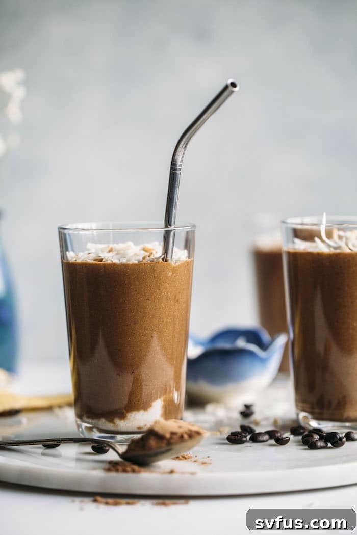 Ingredients for a healthy Toasted Coconut Espresso Smoothie laid out on a table, including a frozen banana, cocoa powder, espresso powder, chia seeds, toasted shredded coconut, coconut oil, vanilla extract, and coconut milk, emphasizing fresh and wholesome components.