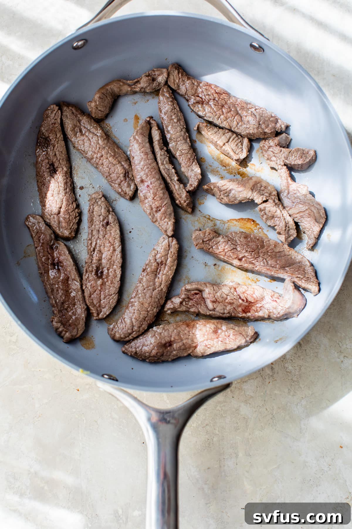 Close-up of perfectly seared strips of flank steak sizzling in a hot skillet, showcasing a beautiful brown crust.