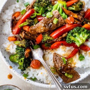 A bowl of rice topped with beef and vegetables like broccoli and red bell pepper