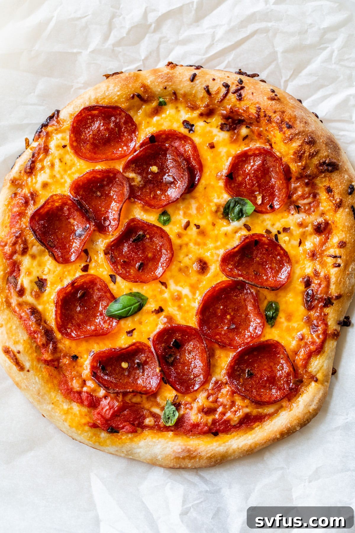 slice of pepperoni pizza on a piece of parchment paper, showing the crispy crust
