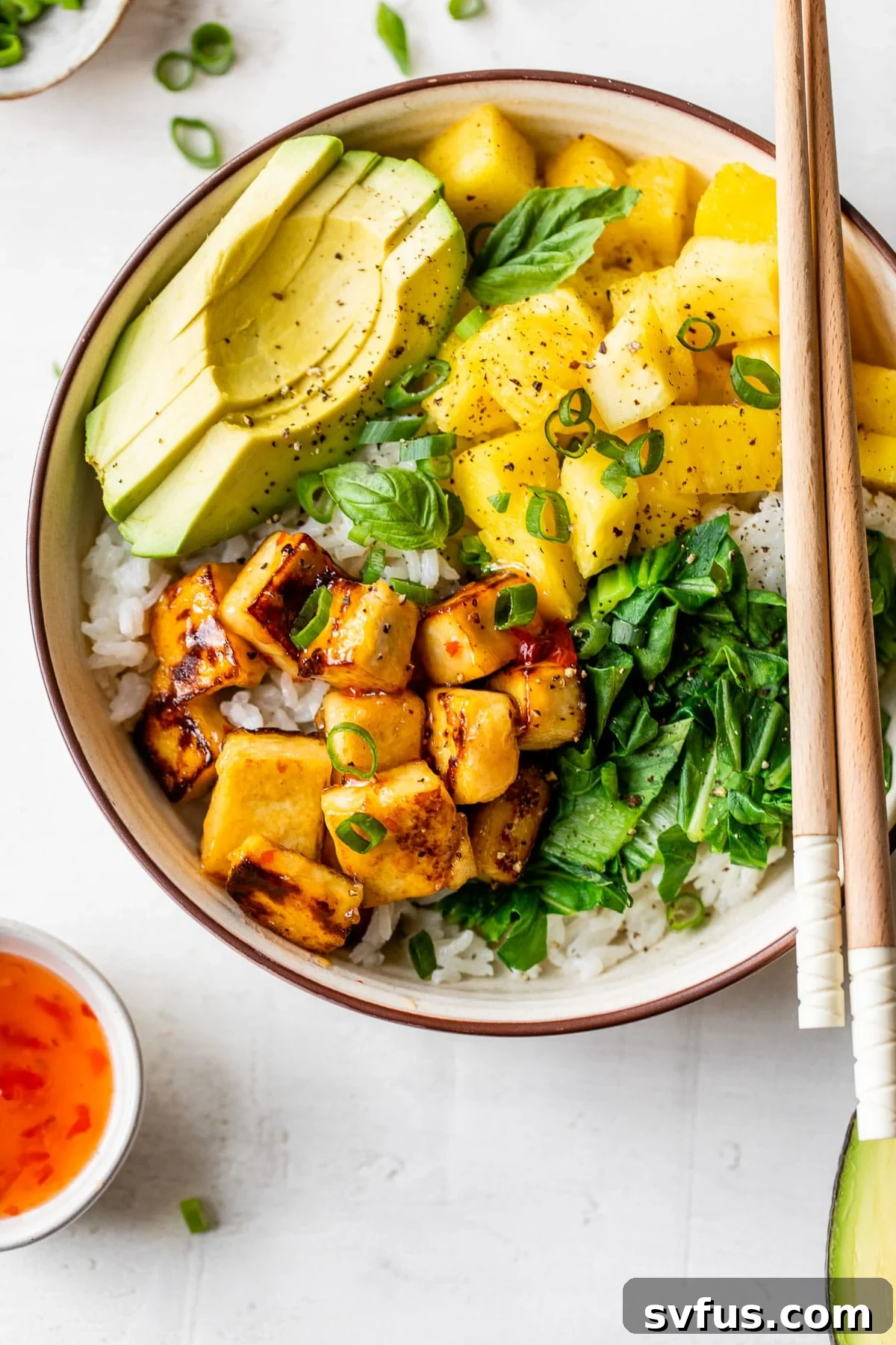 A beautifully arranged bowl with creamy white coconut rice, golden crispy tofu cubes, vibrant pineapple chunks, and sliced avocado, garnished with fresh herbs.