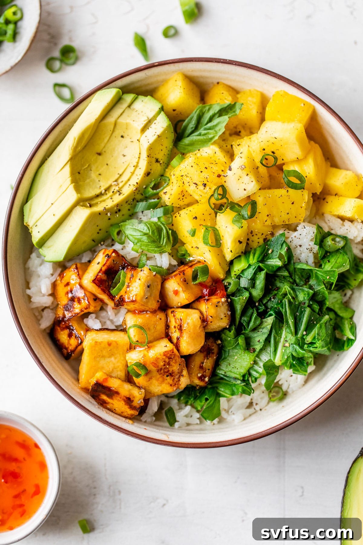 A vibrant rice bowl generously topped with diced pineapple, creamy avocado slices, and golden, crispy diced tofu, showcasing fresh and colorful ingredients.